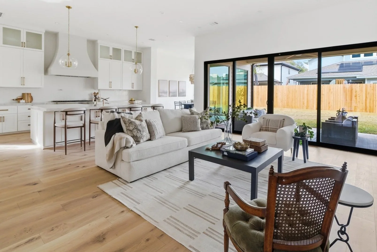 Open-concept living room with white sofa, armchair, black coffee table, and sliding glass doors leading to backyard.