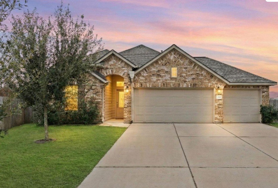 A suburban house with a three-car garage, brick exterior, front door, and landscaped yard during sunset.