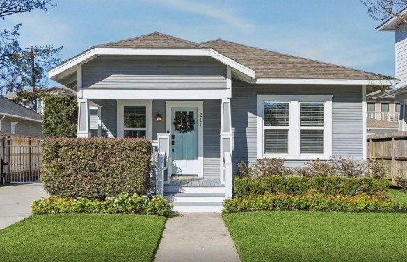 Front view of a blue house with a small porch, decorated with a wreath on the door, surrounded by a well-manicured lawn and garden.