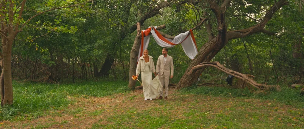 Abby and Daniel walking together beneath the trees after their ceremony.