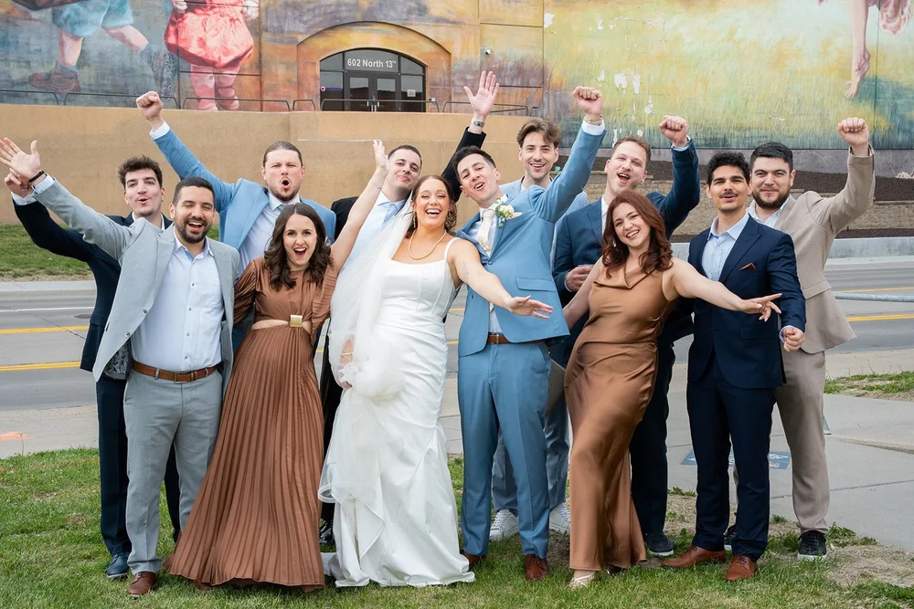 Grace and Alex with their wedding party beside a colorful downtown Omaha mural.