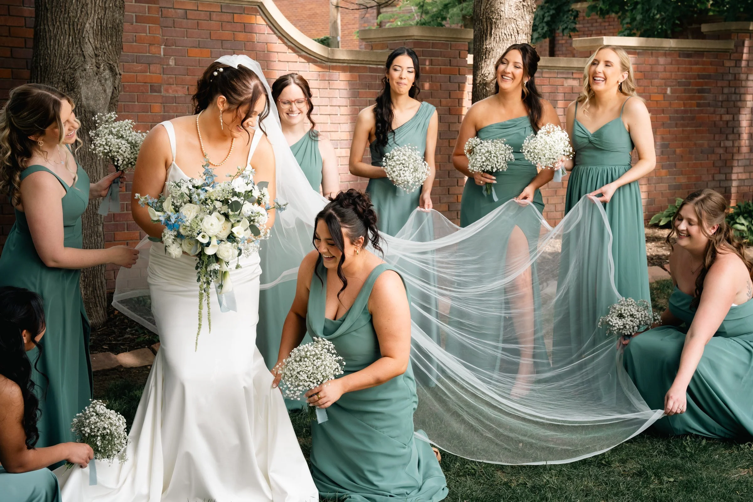 Grace and her bridesmaids laughing beneath her veil at the Gerald R. Ford Birthsite gardens in Omaha.