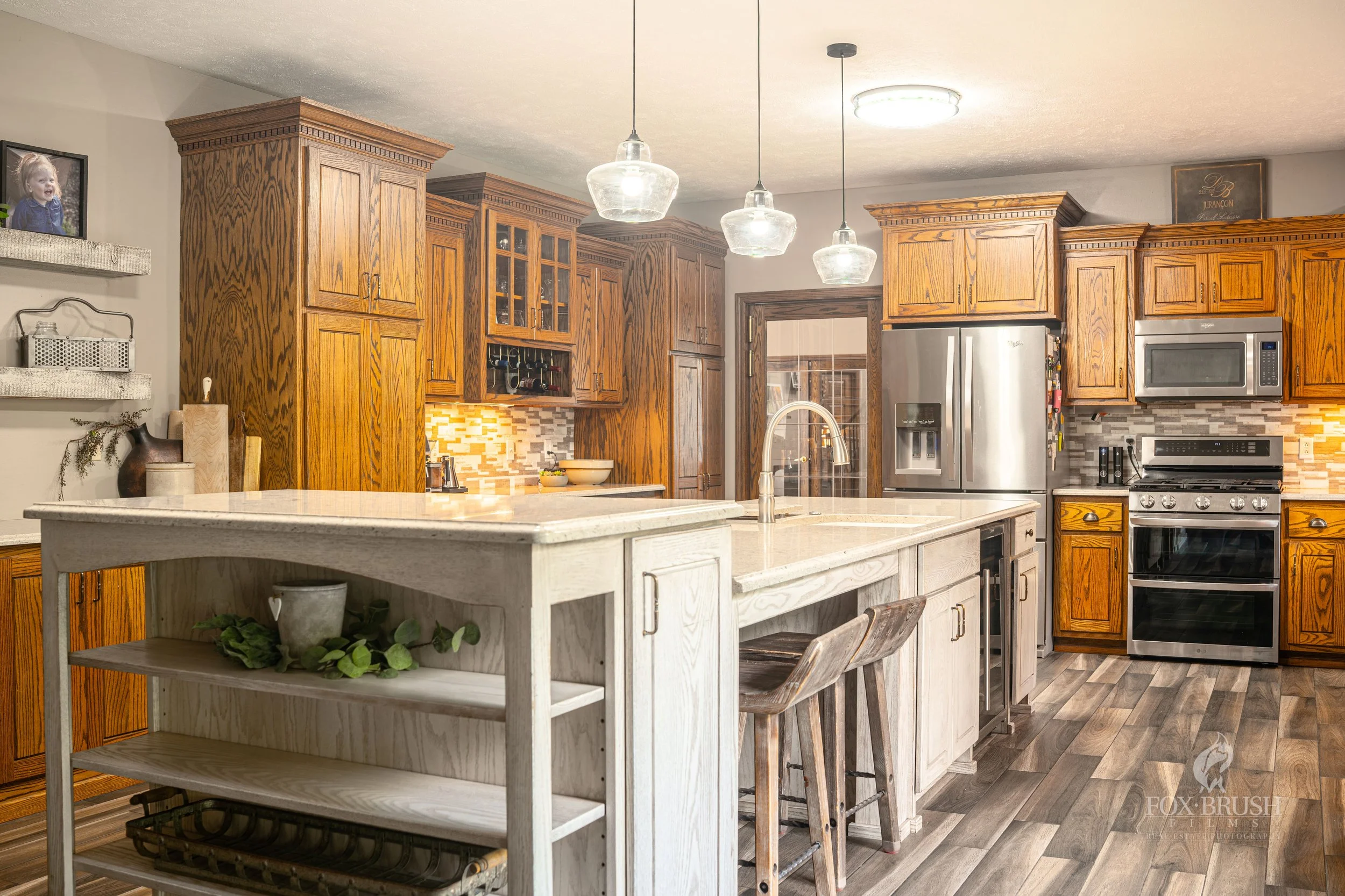 Kitchen with wooden cabinets, stainless steel appliances, a white island with a sink, and a wood floor.
