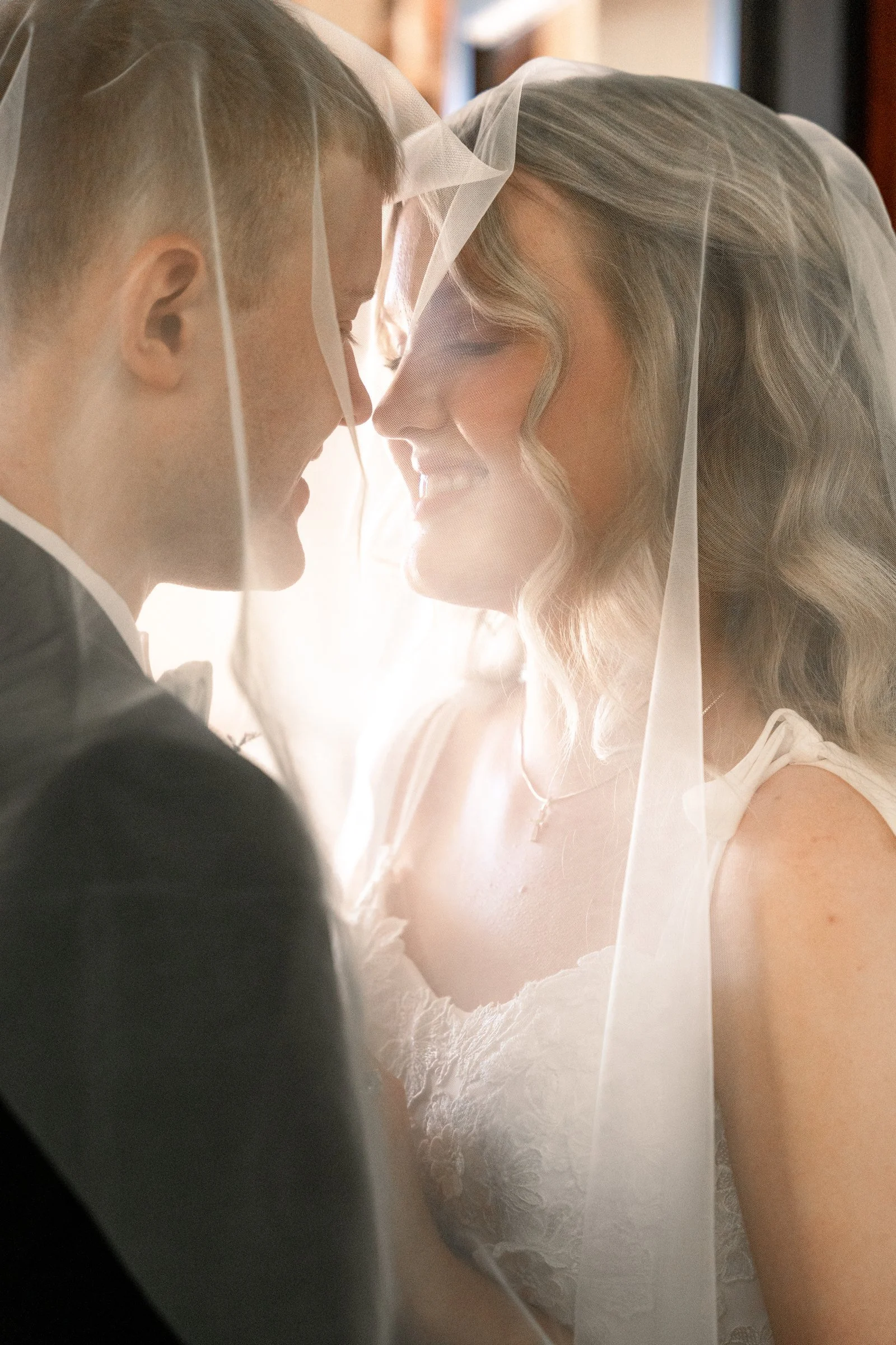 Bride and groom smiling close together beneath the bride's veil.