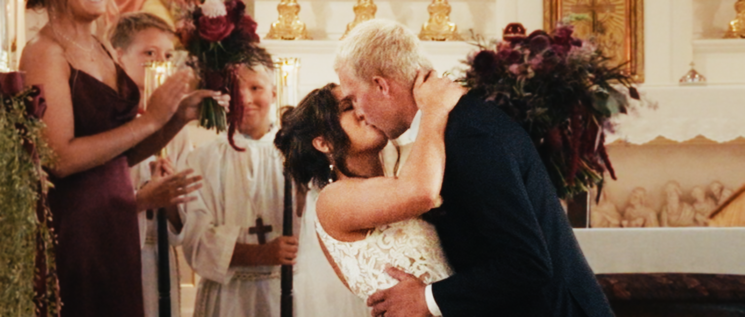 Newlyweds sharing their first kiss at the church altar as the wedding party applauds