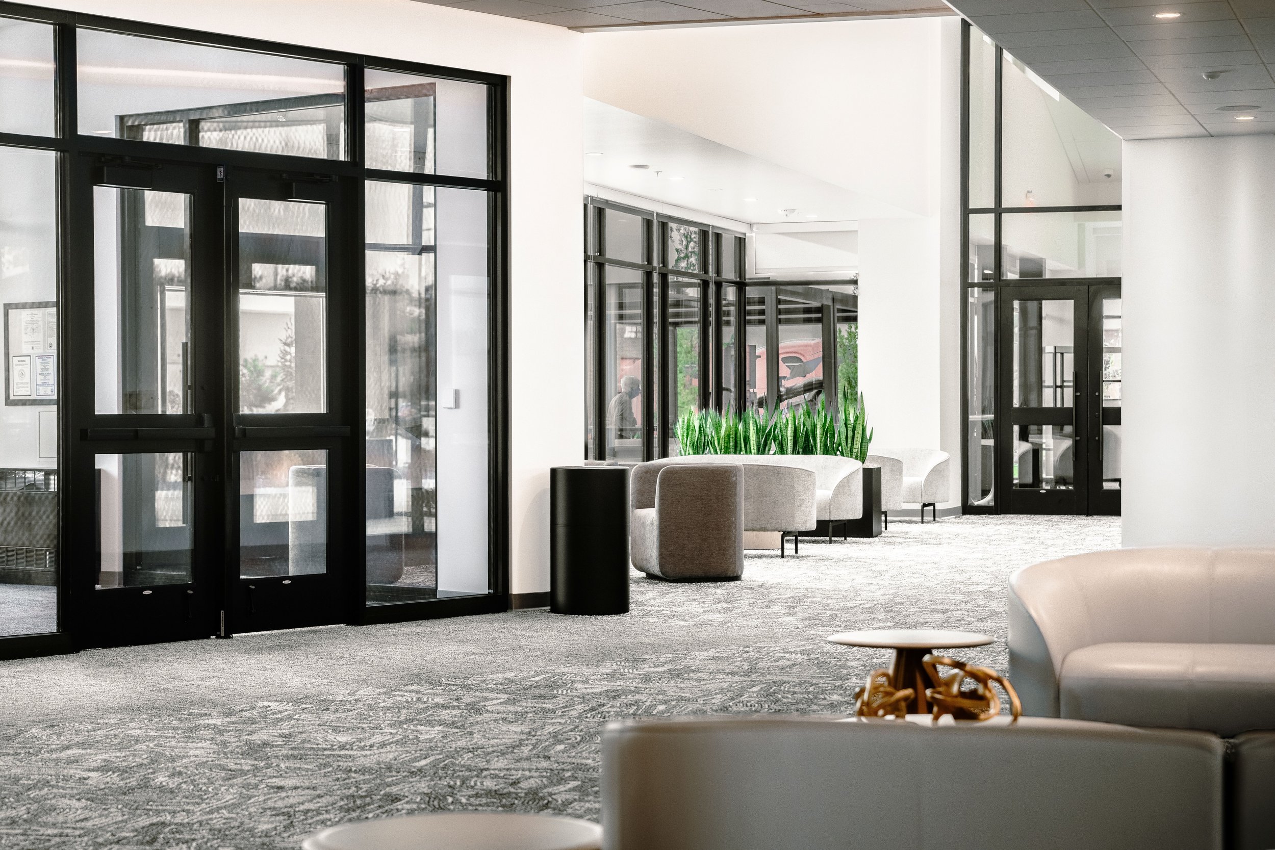 Modern hotel lobby with glass doors, seating area, and decorative plants.