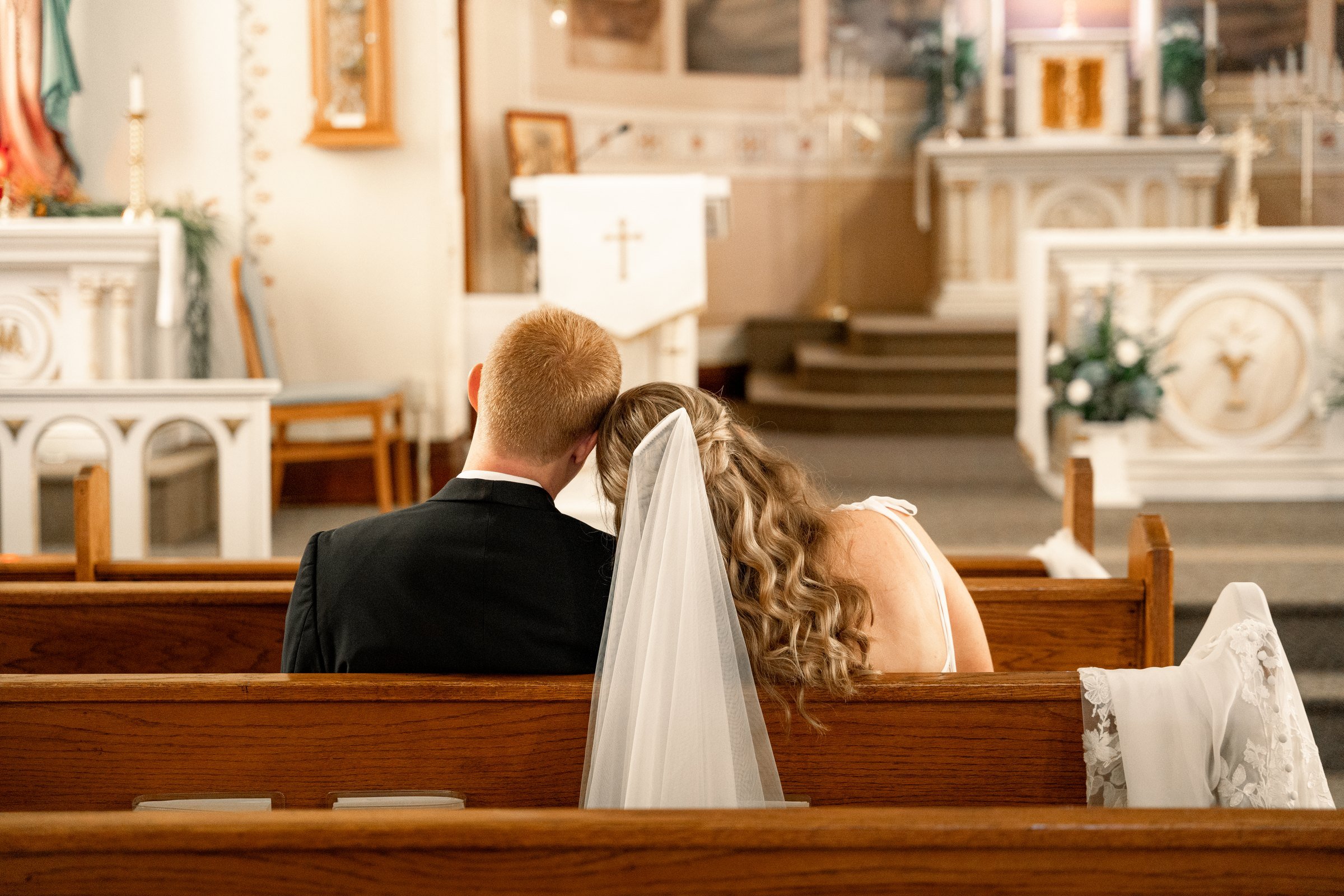 Bride and groom sharing a quiet moment in a wooden church pew at their Northeast Nebraska Catholic wedding.