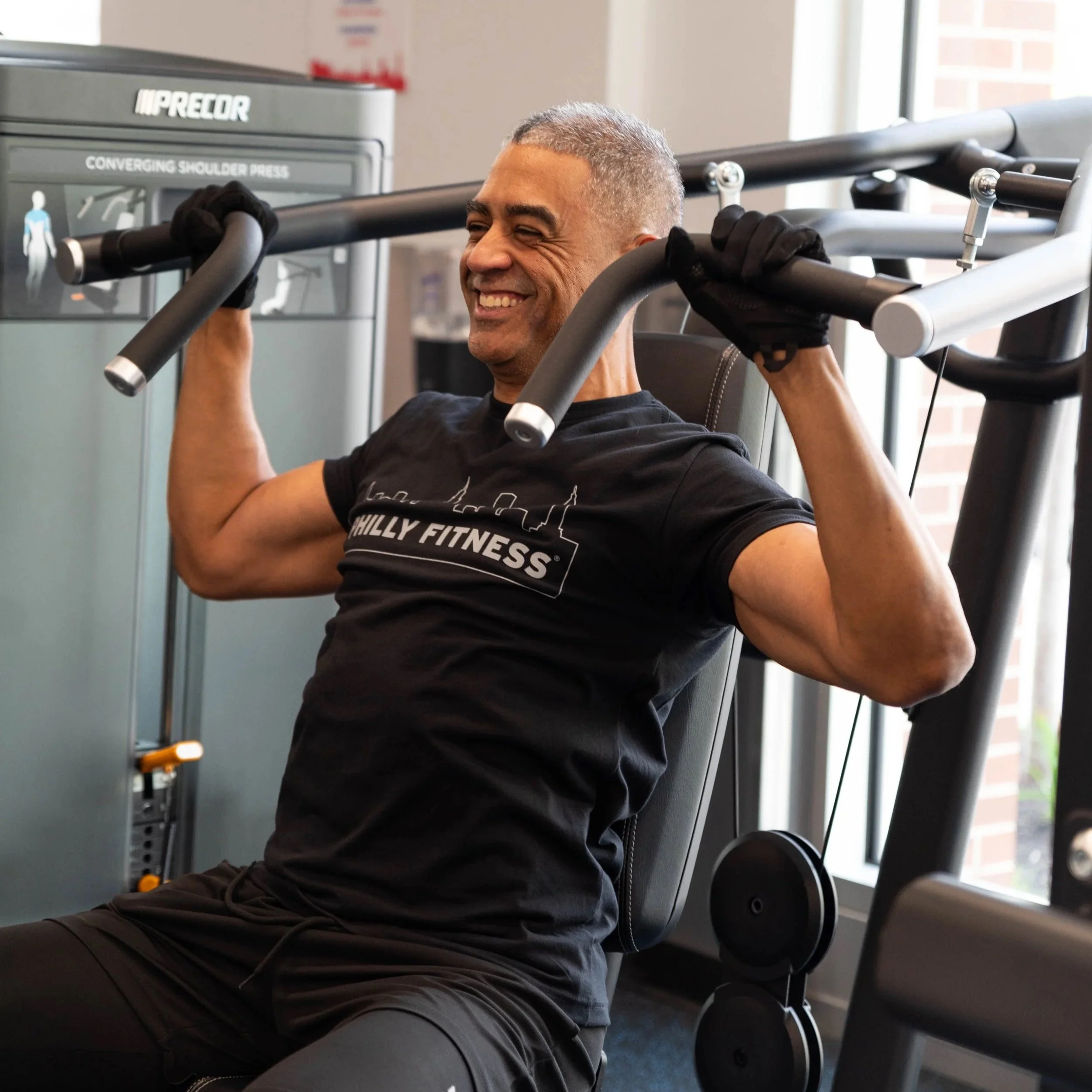 Happy gym member on a weight machine in a Philly Fitness® Balck Skyline T-Shirt
