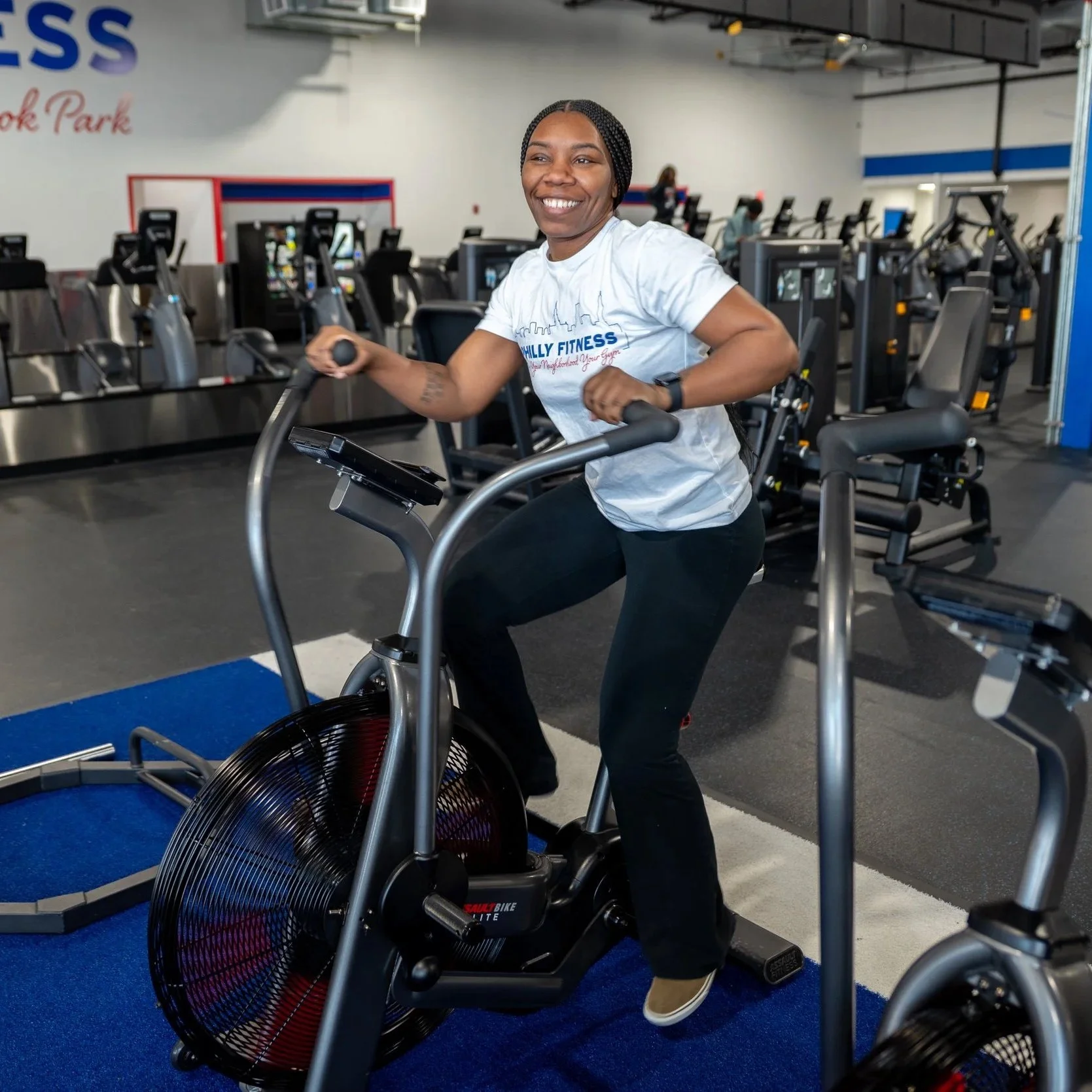 Gym member riding the bike with their White Philly Fitness® Skyline T-Shirt on