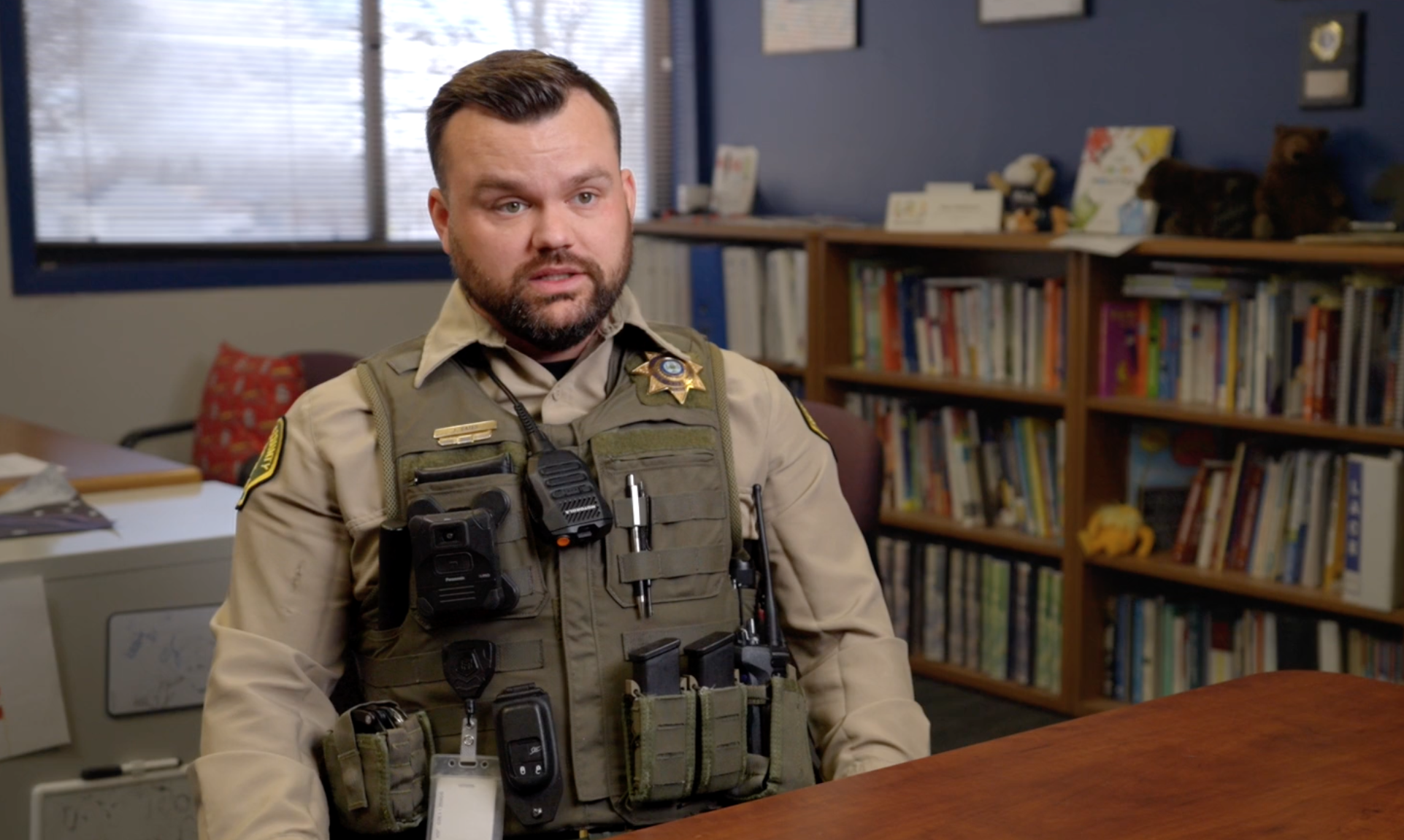 Uniformed law enforcement officer being interviewed in front of a bookshelf for the GeoComm school safety film