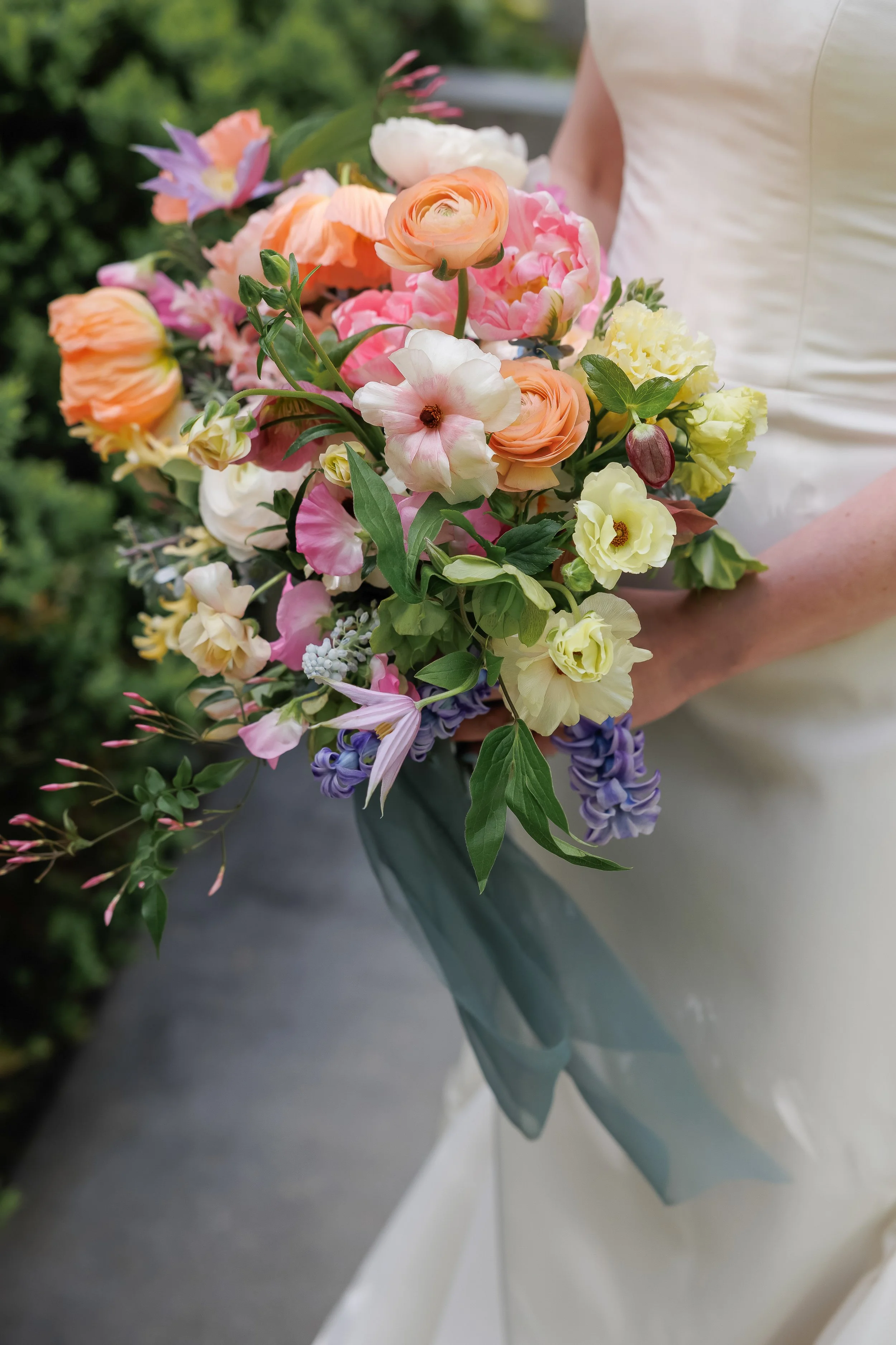 A person in a white dress holding a colorful bouquet of flowers with various blooms and green foliage.