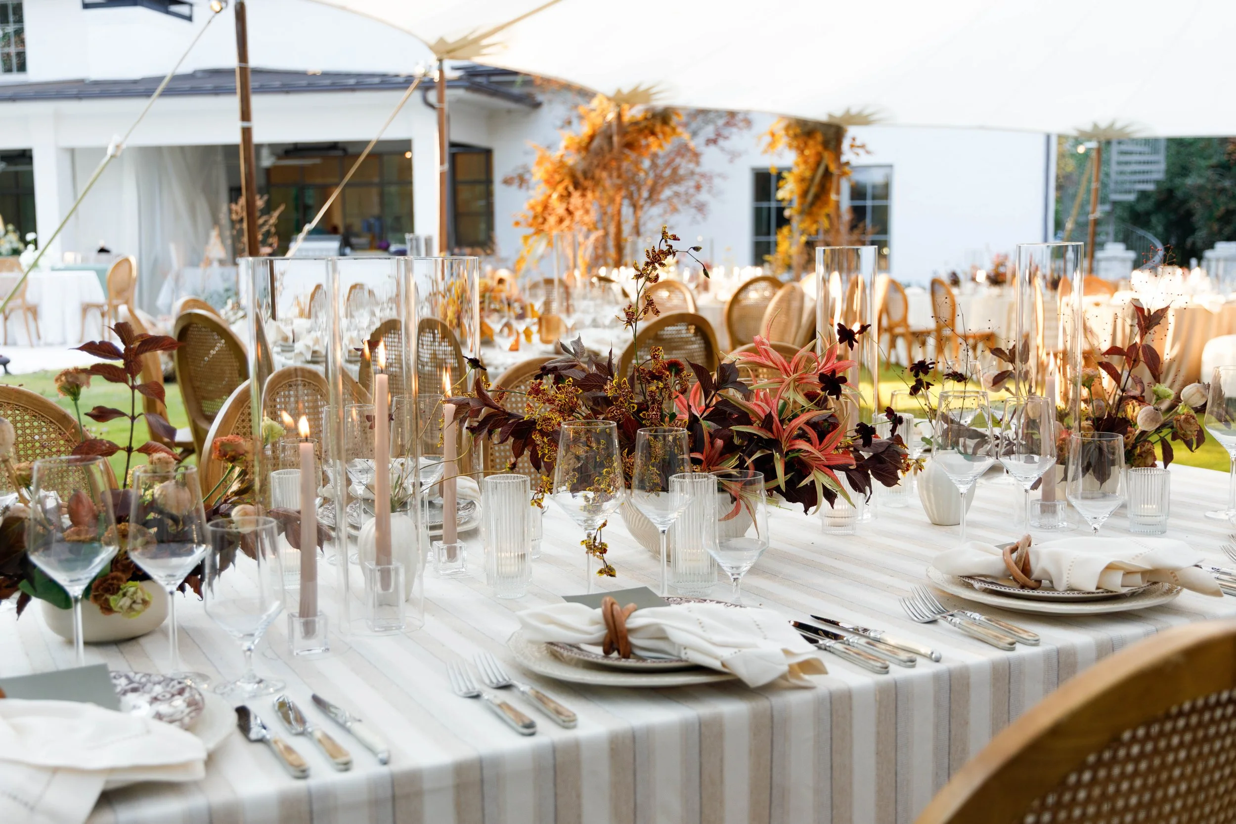 Elegant outdoor dining table decorated with floral centerpieces, candles, glassware, and place settings, set for a special event or wedding reception.