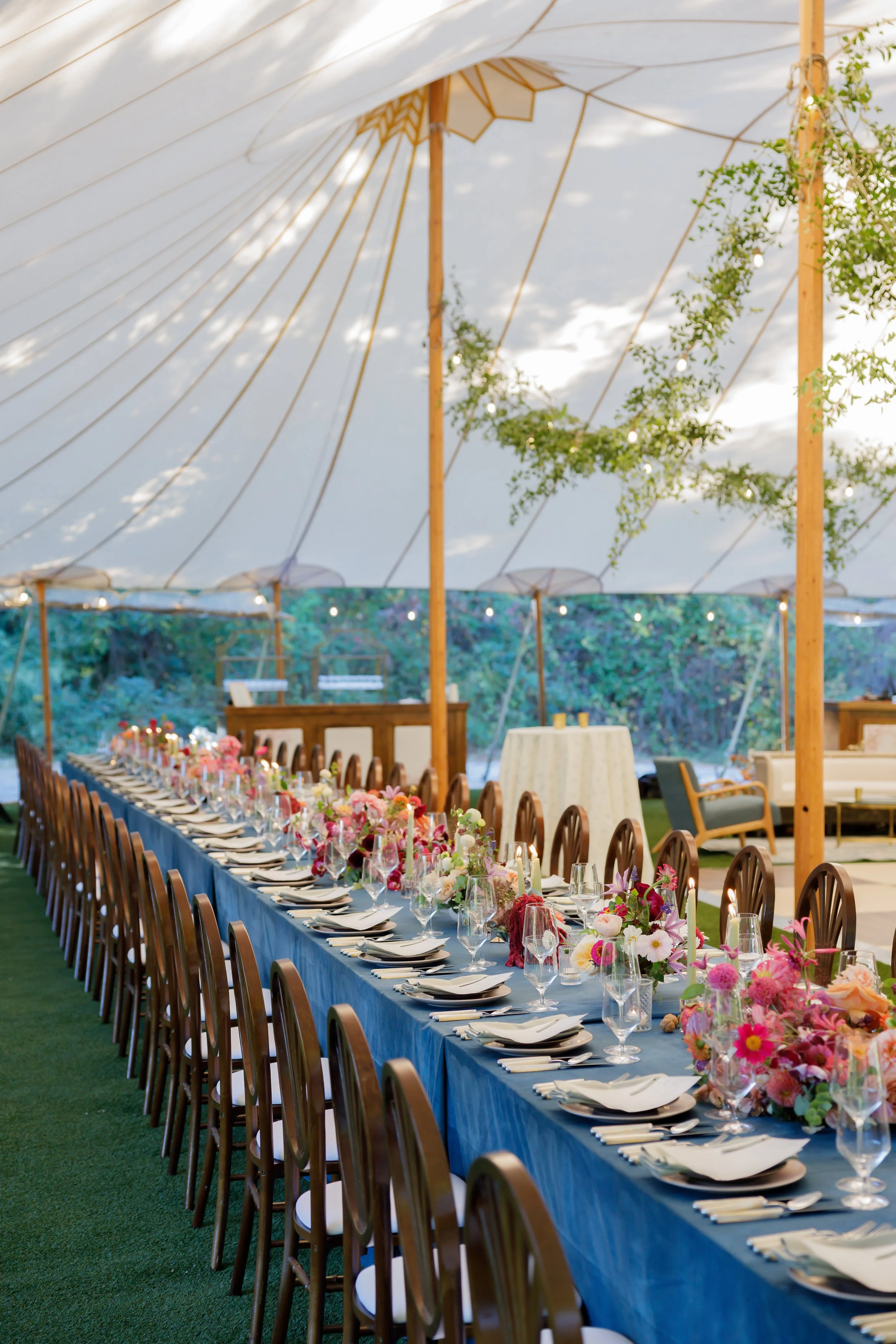 Long outdoor dining table with floral centerpieces under a large white tent.