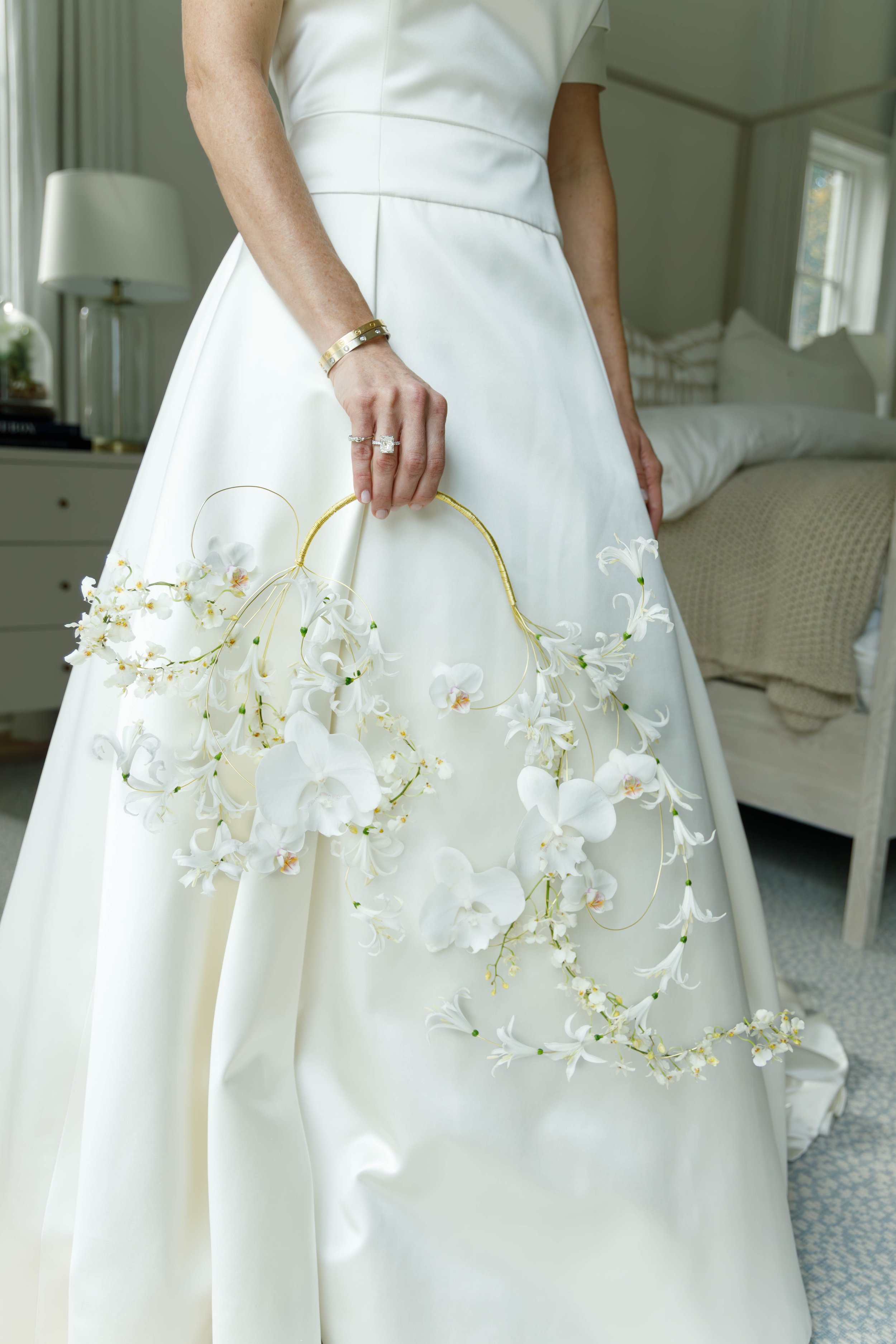 A woman in a white wedding dress holding a floral crown of white orchids.
