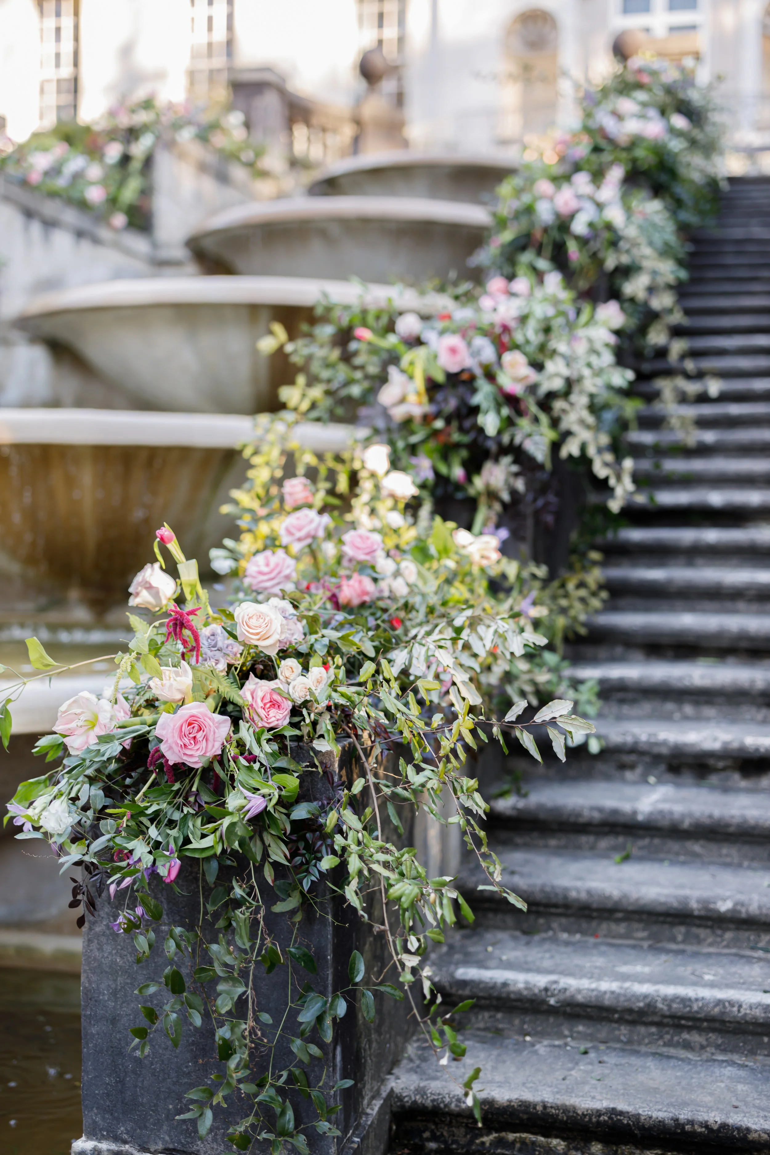 Stone staircase with flower arrangements along the side, leading up to a building with ornate architecture and fountains.
