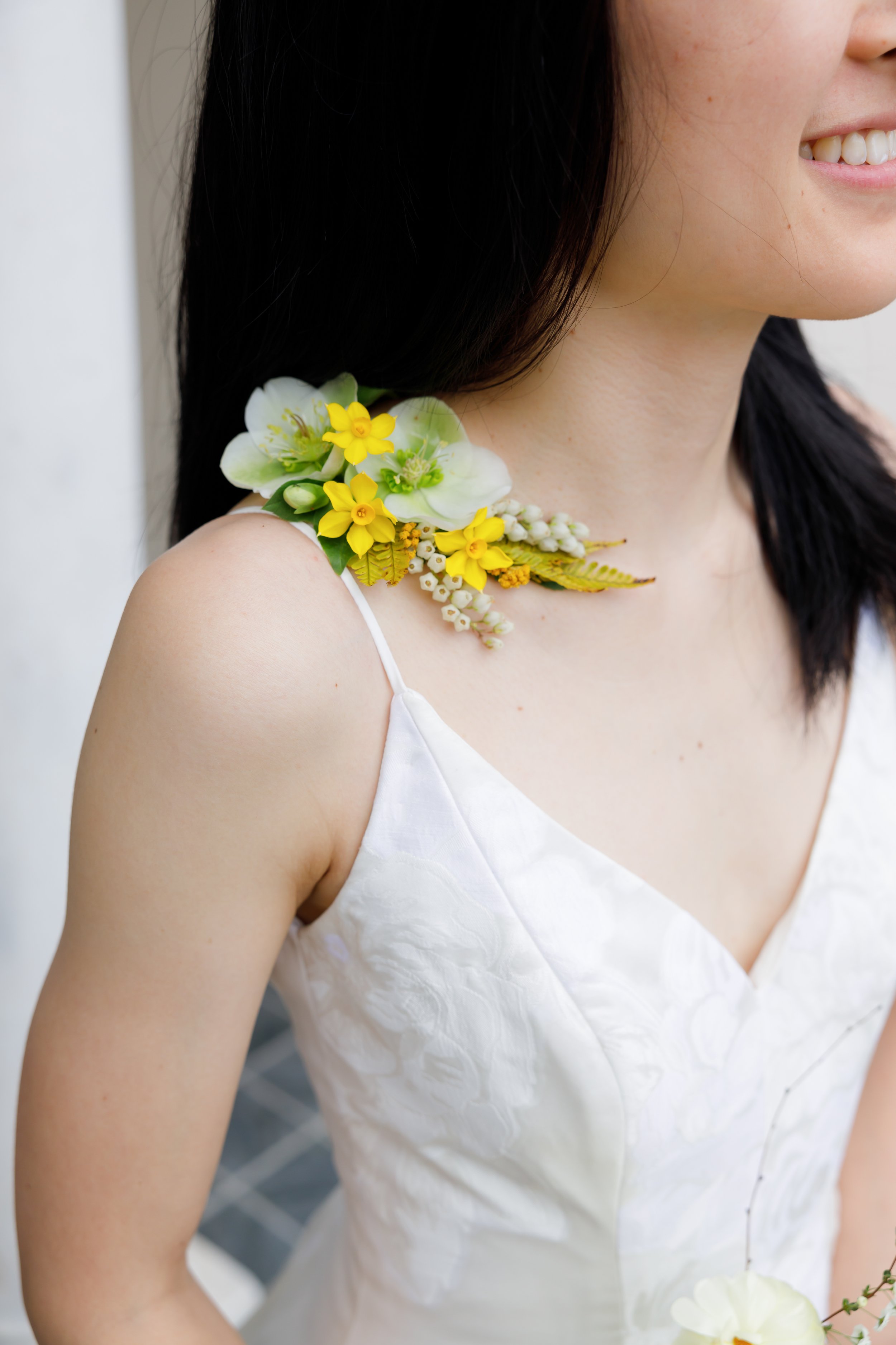 Close-up of a woman wearing a white wedding dress with a floral shoulder accessory.