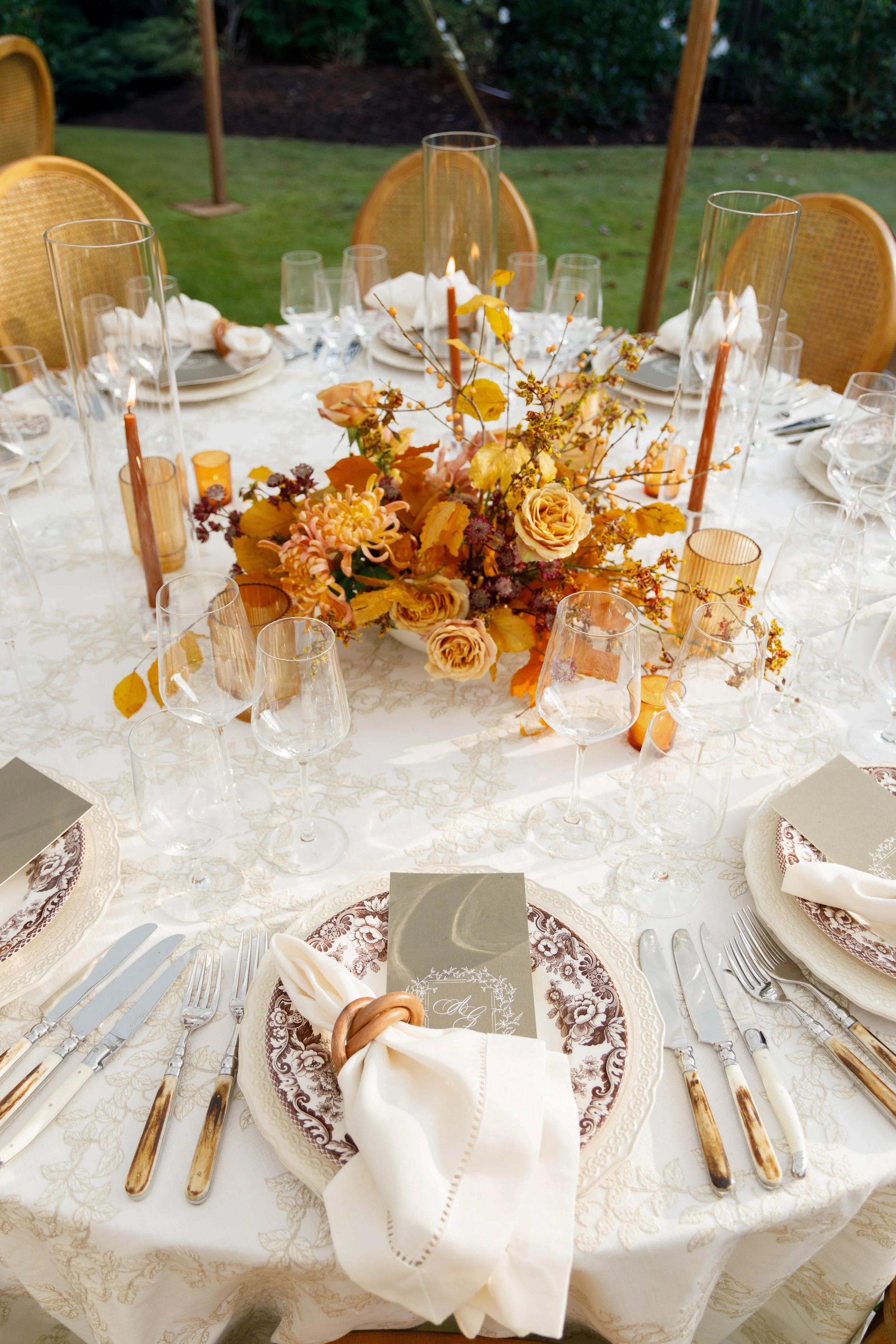 Elegant outdoor dining table set with floral centerpiece, glassware, plates, and cutlery, prepared for a formal event or celebration.