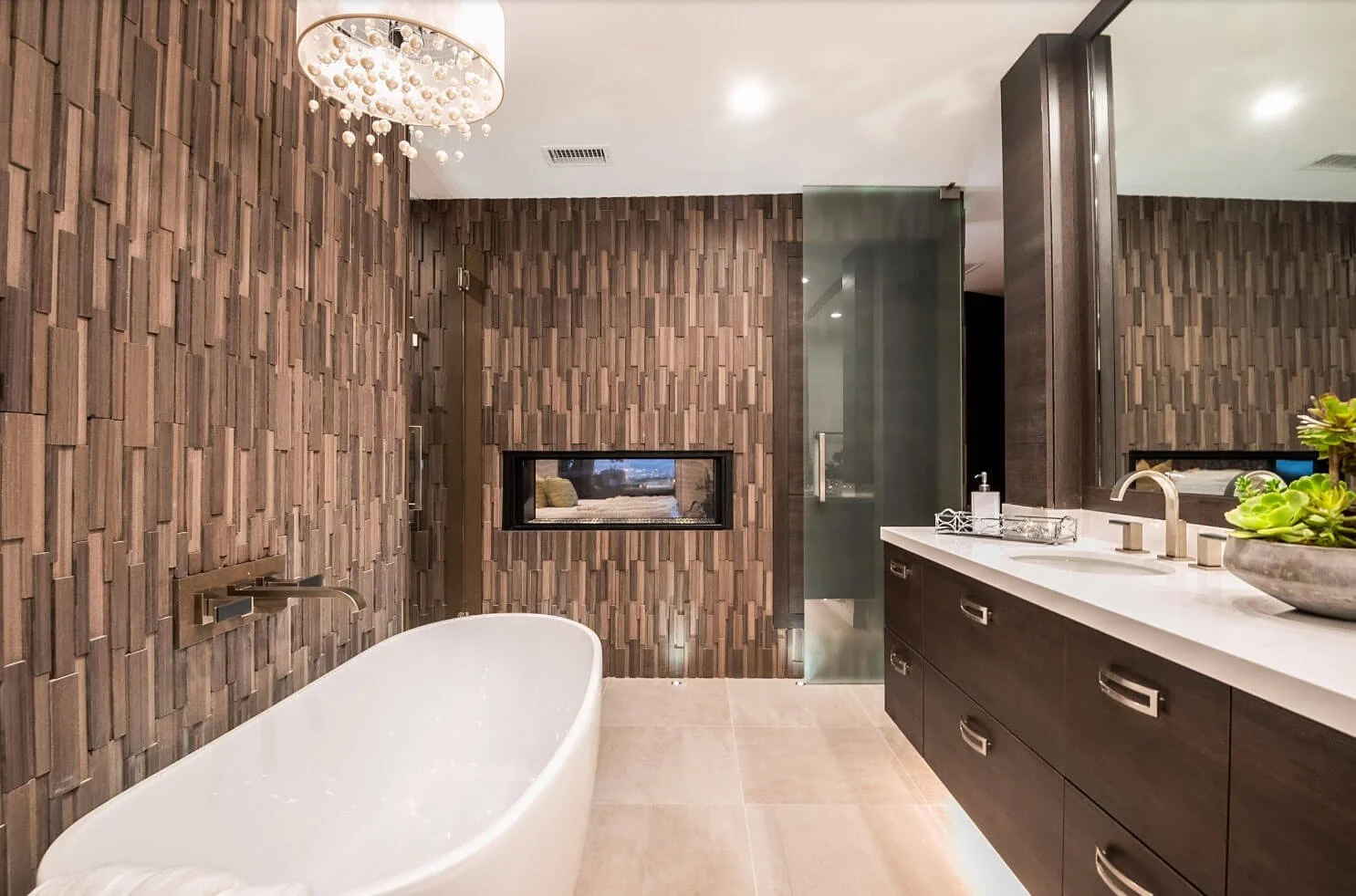Modern bathroom with a freestanding white bathtub, wooden textured wall, glass shower enclosure, dark wood vanity with white countertop, potted succulent, and a small window.
