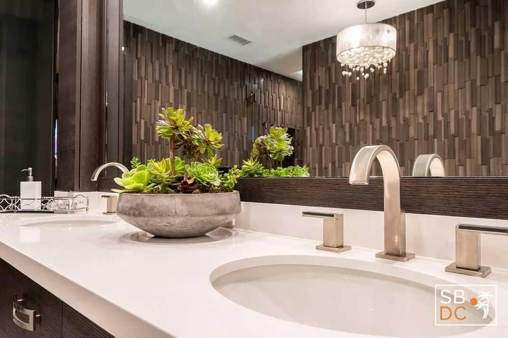 Modern bathroom sink with a large concrete planter filled with succulents, dark wood cabinets and a textured wood-paneled wall, large mirror, white countertop, and a decorative chandelier.