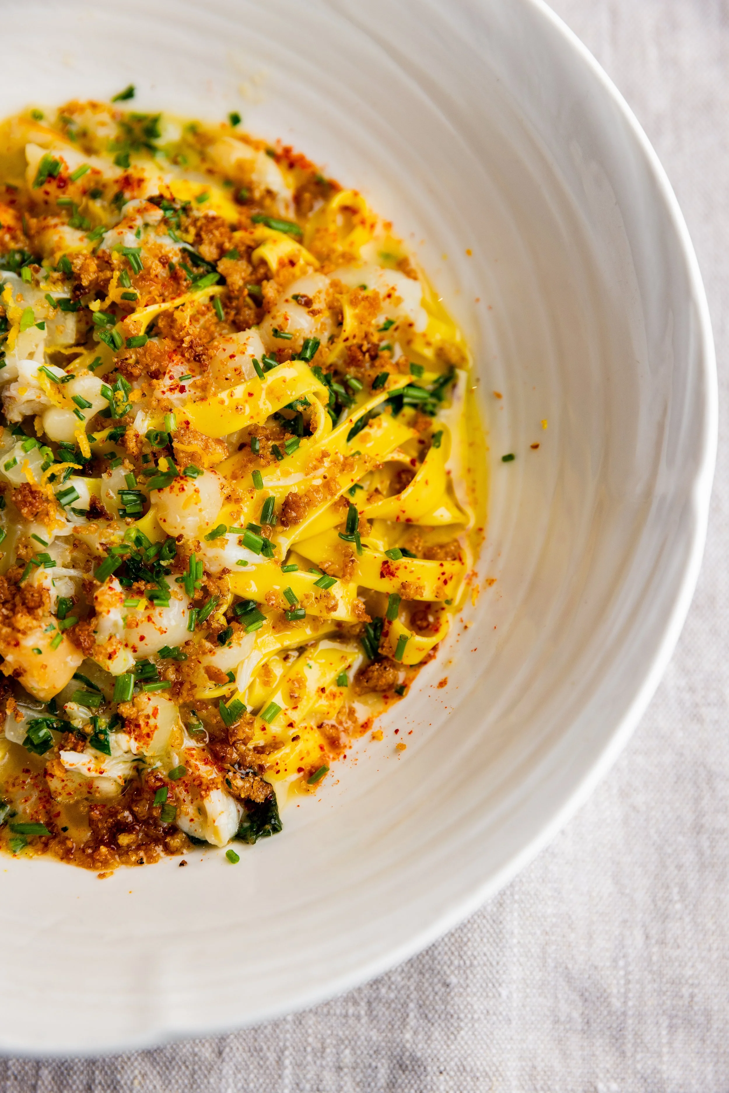 Close-up of a bowl of creamy scrambled eggs sprinkled with chopped chives and paprika, on a light-colored fabric surface.
