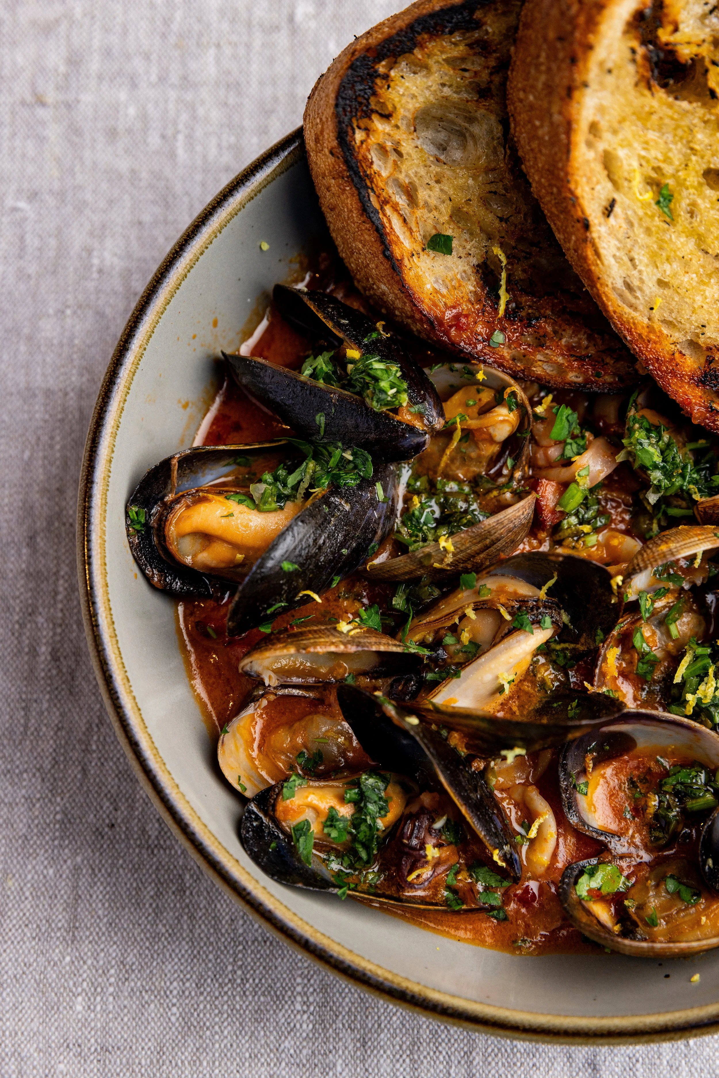 Bowl of steamed mussels in tomato broth garnished with chopped parsley, served with toasted bread slices