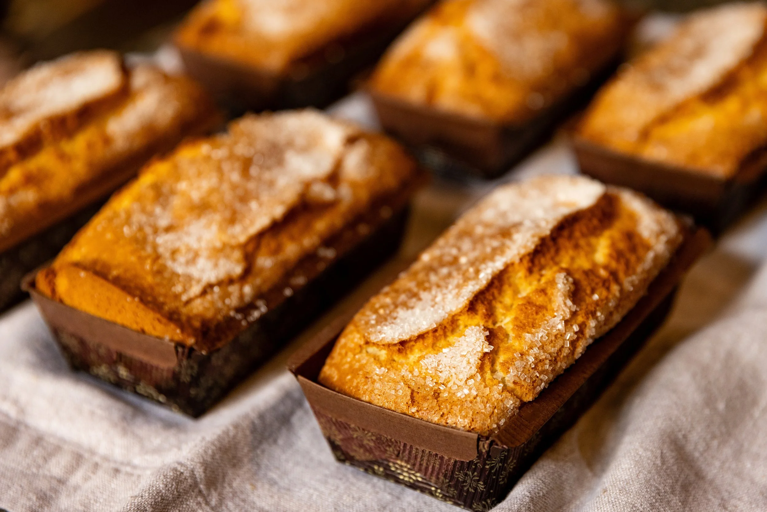 Close-up of freshly baked banana bread slices with sugar, placed in paper baking cups on a cloth surface.