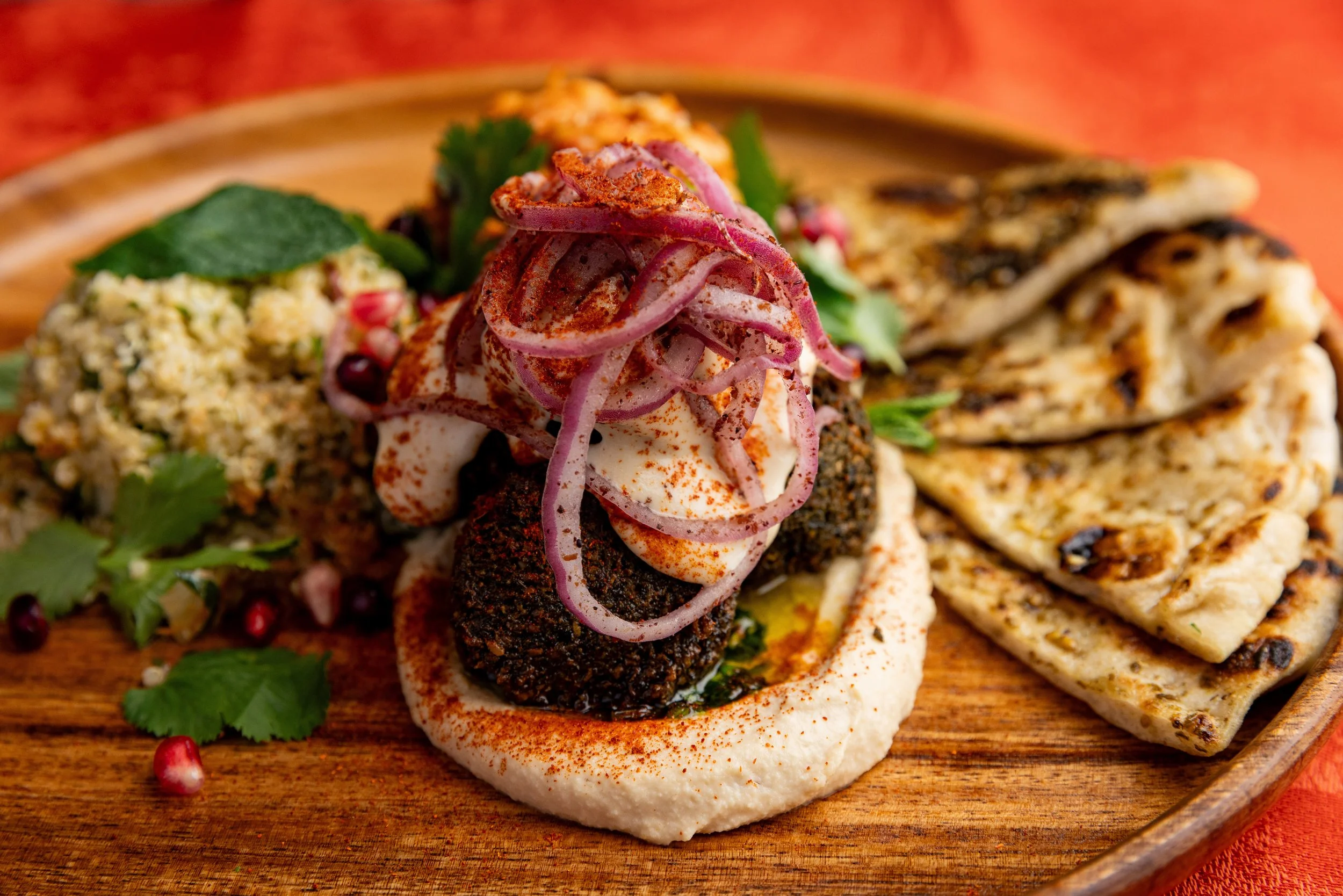 Plate of Middle Eastern food with hummus, grilled flatbread, and roasted chickpeas, garnished with herbs and red onion.