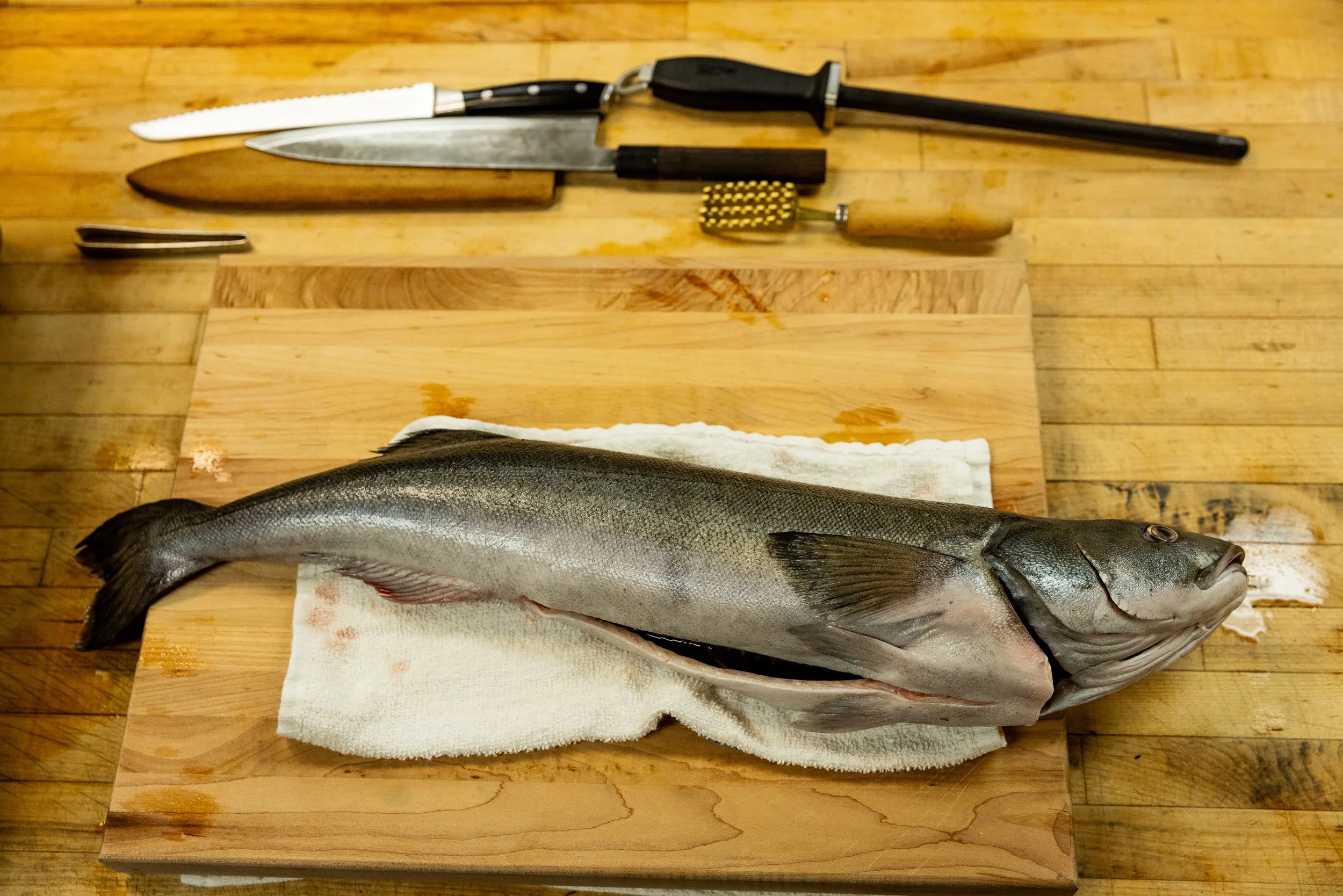 Freshly caught fish on a wooden cutting board with knives and a meat tenderizer above it.