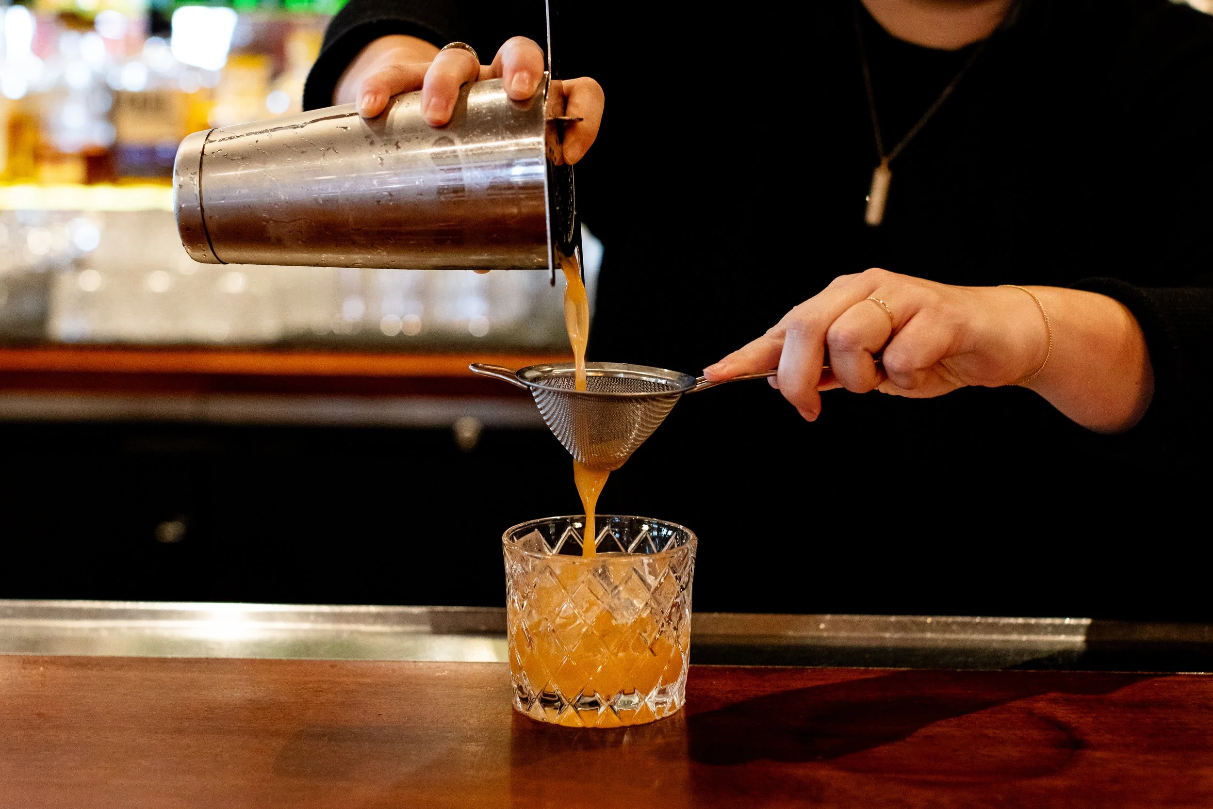 Person pouring a cocktail through a strainer into a glass