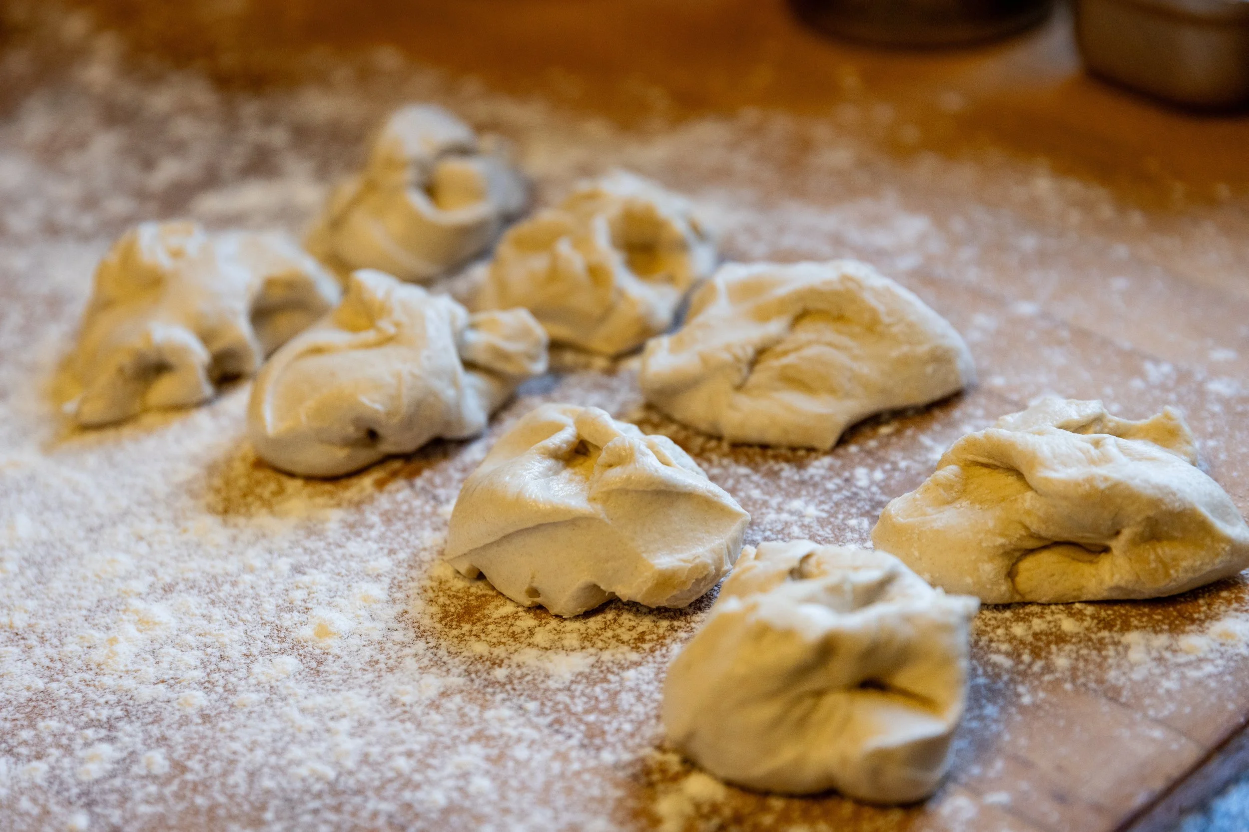 Uncooked dumplings or pasta is arranged on a floured wooden surface.