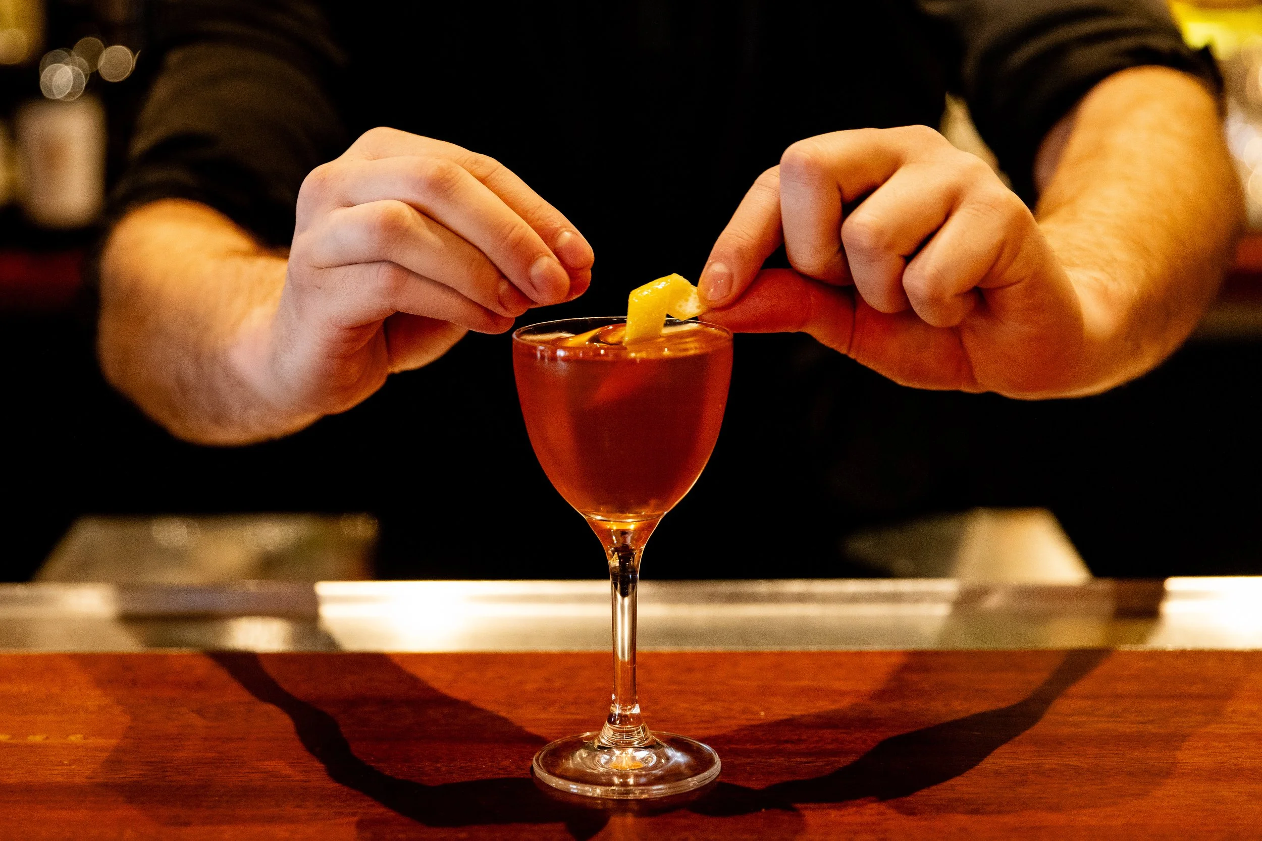 A bartender garnishing a cocktail with a lemon wedge.
