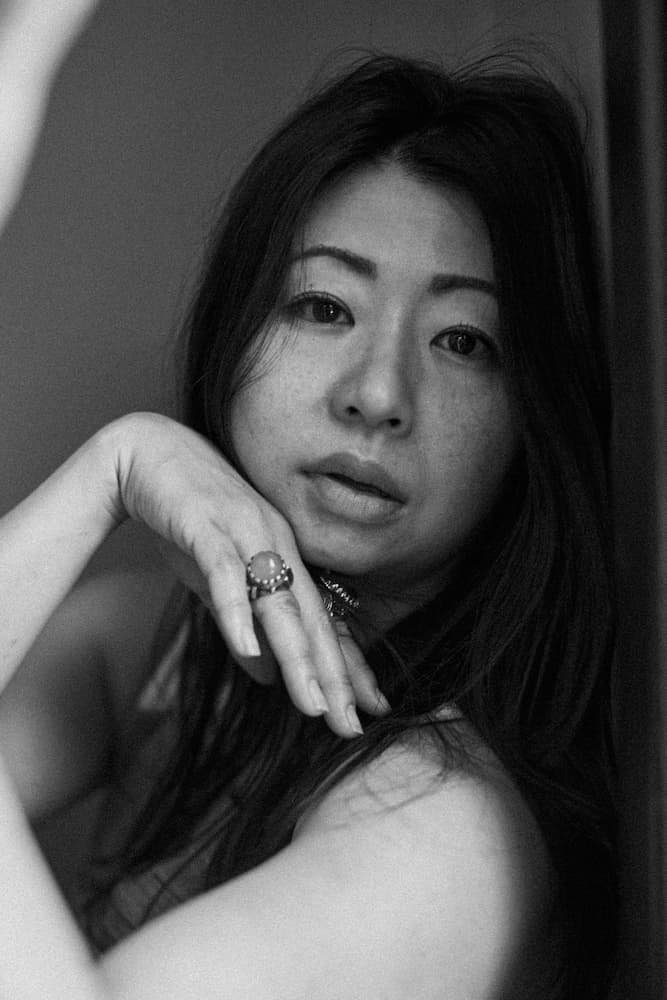 Black and white portrait of a woman with long hair, resting her chin on her hand, wearing a ring.