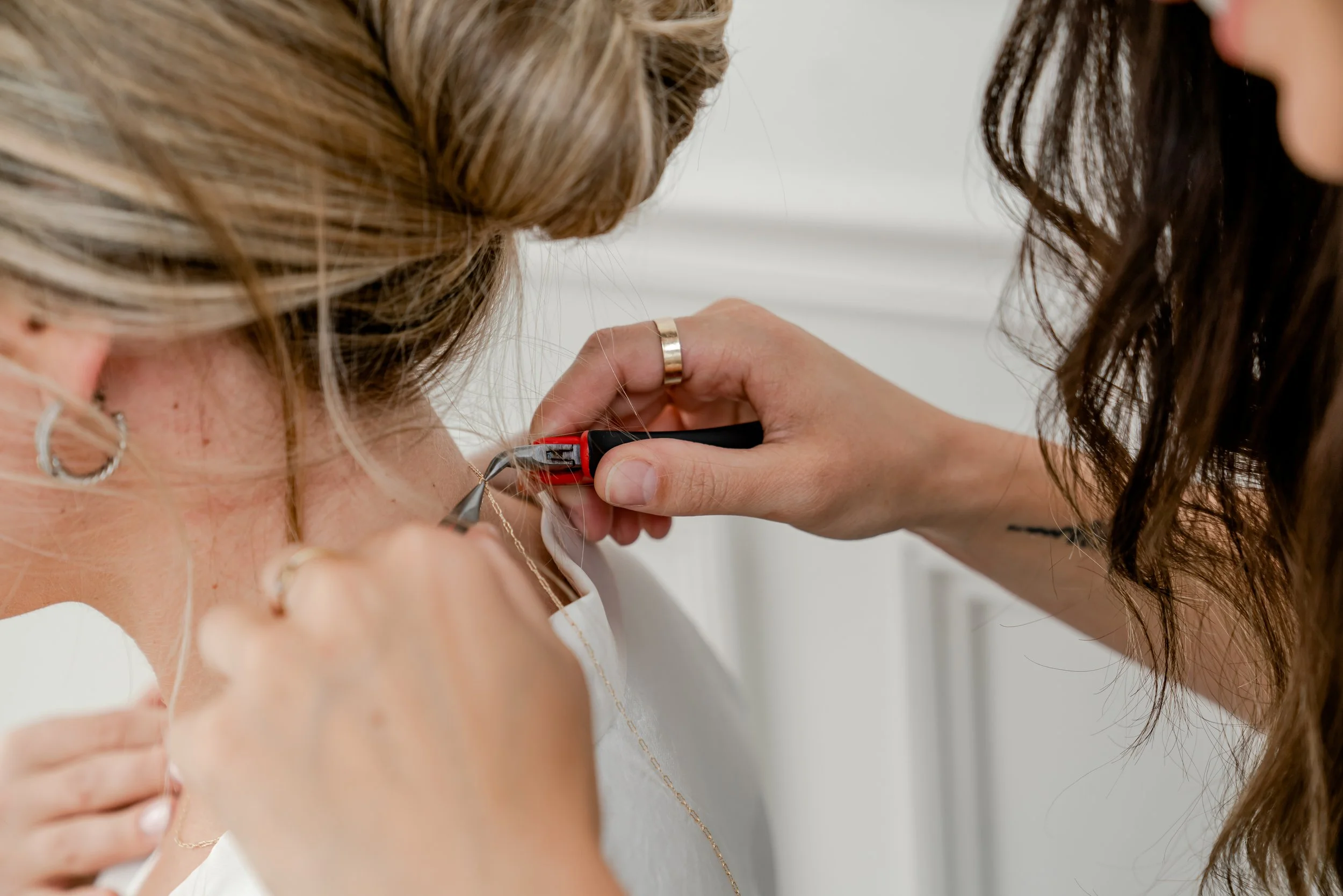 A person is using wire cutters to cut a necklace around a woman's neck, with a focus on hands and jewelry.