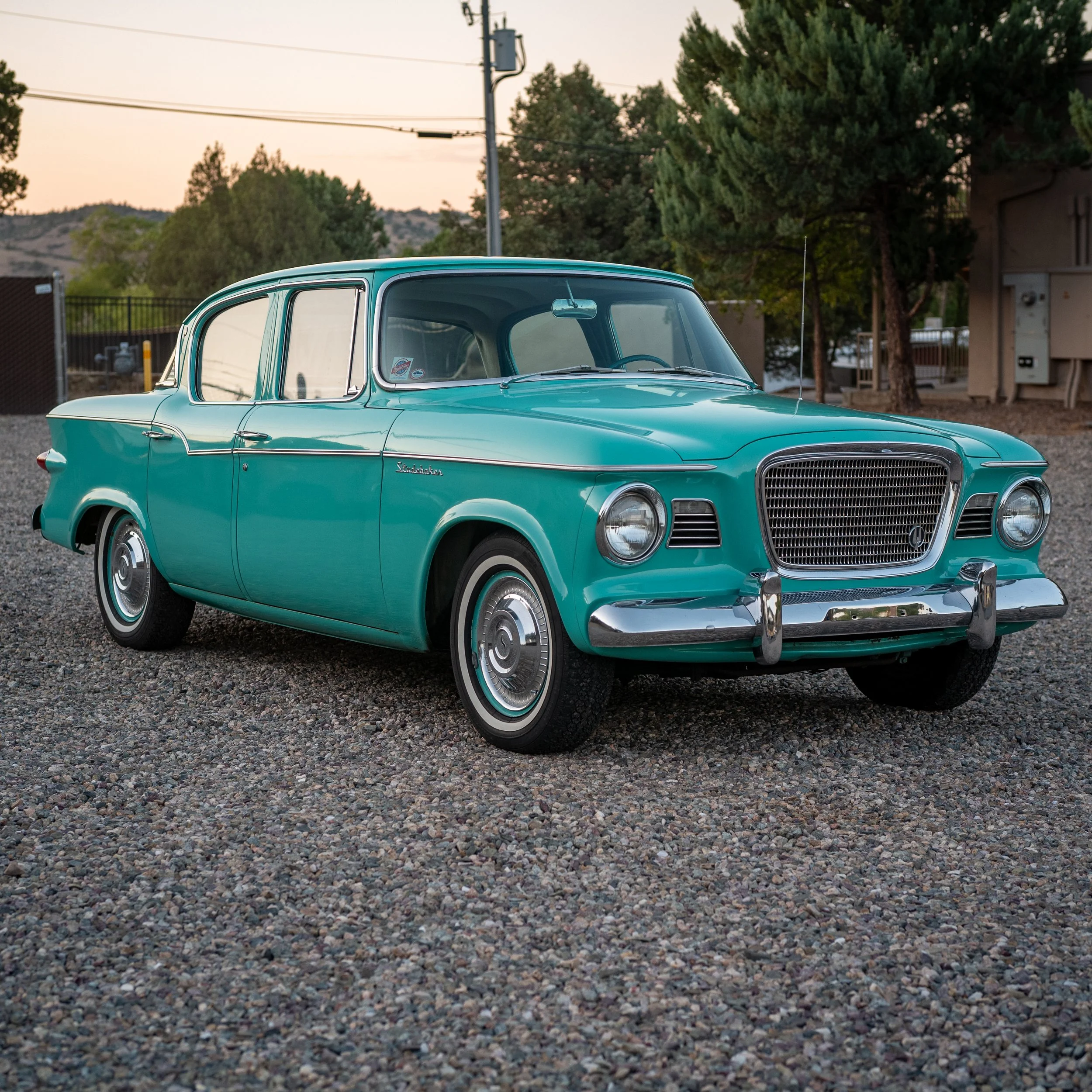 A vintage teal station wagon car parked on a gravel lot during sunset.