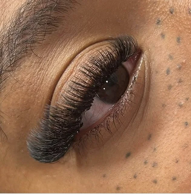 Close-up of a person's eye with long, thick false eyelashes and small dark freckles on the skin near the eye.