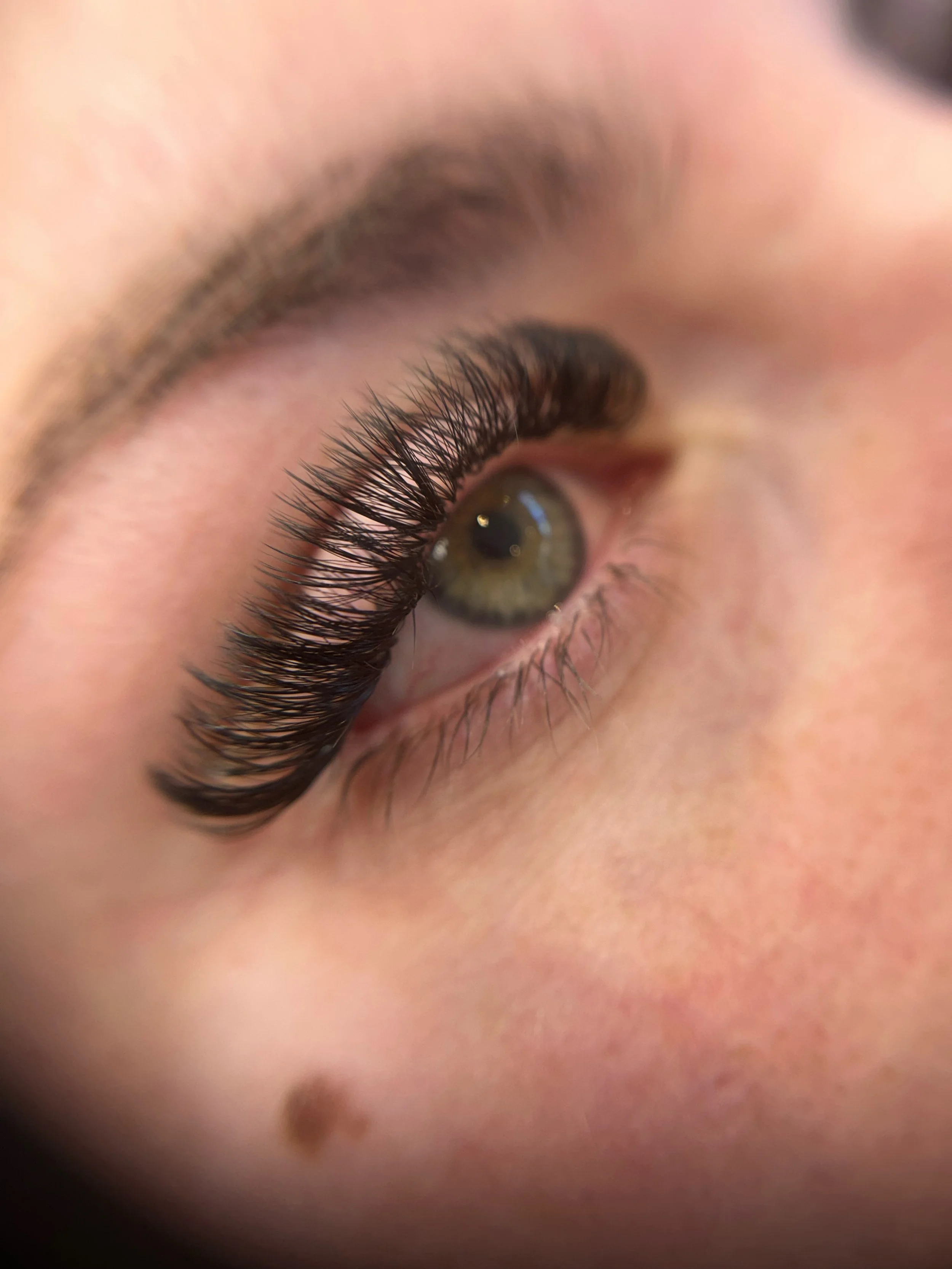 Close-up of a human eye with long, curled eyelashes and a melting snowflake on the eyelid.
