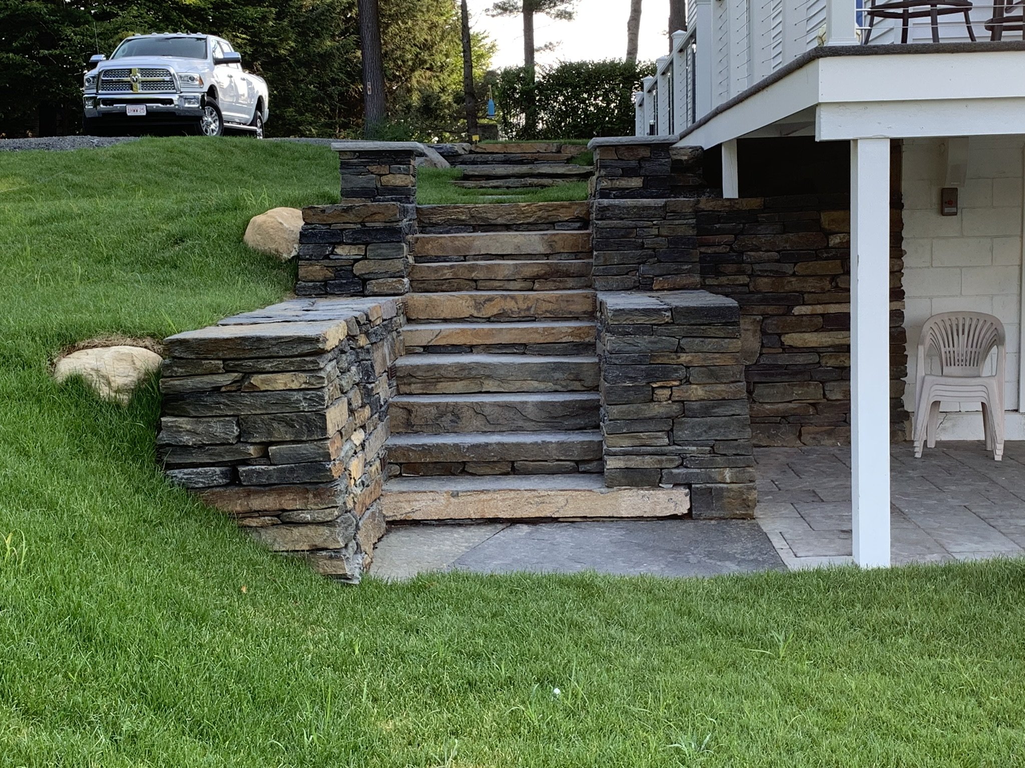 The tight corners of these retaining walls demonstrate precision in design, creating a visually appealing and structurally sound boundary. Introducing a staircase crafted from the same Goshen stone, the walls become an integral part of a practical an