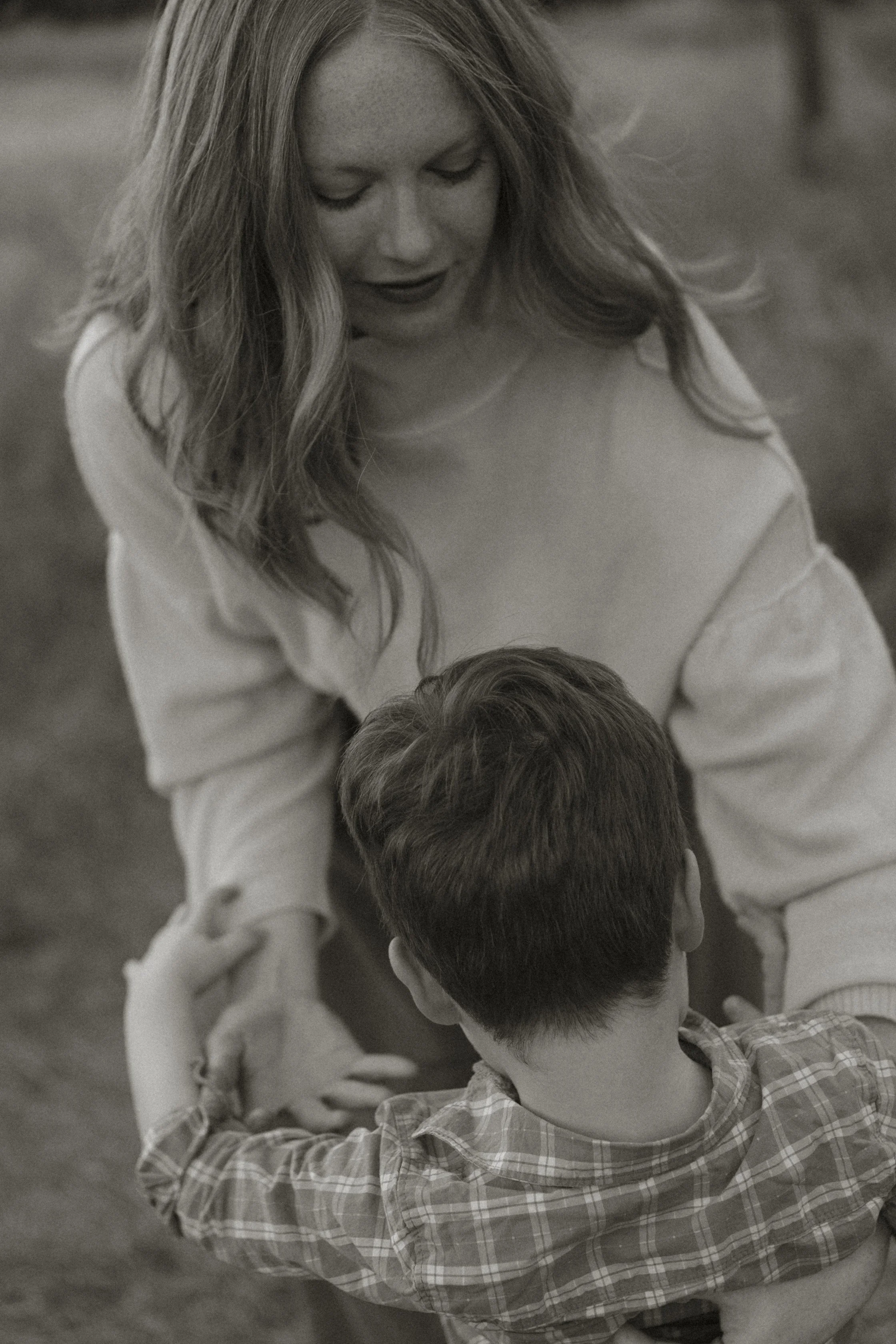 Mother gently holding her young child’s hands during a quiet, candid moment at an outdoor family photography session