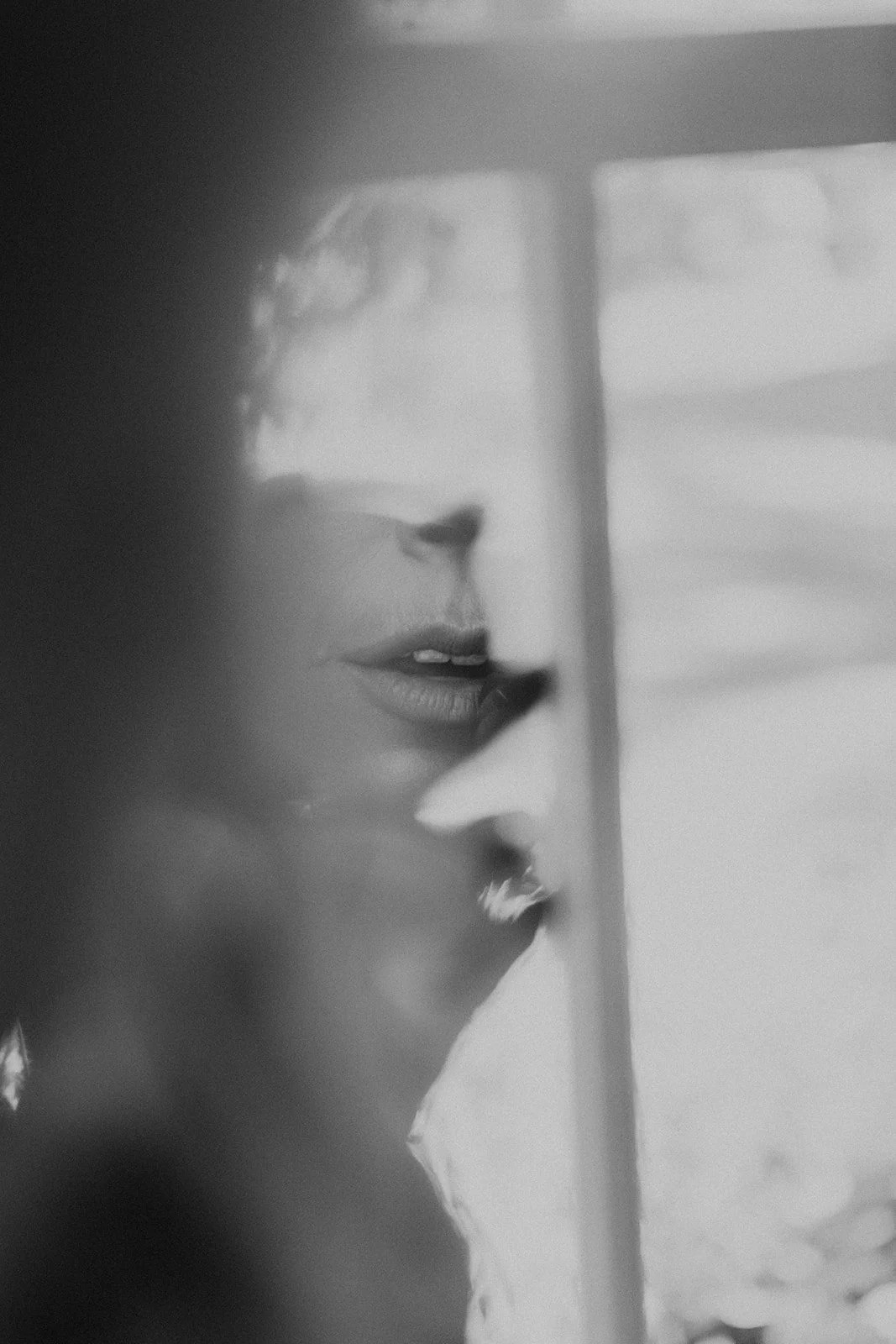 Black and white photo of a woman with curly hair, seen in profile through a glass window.
