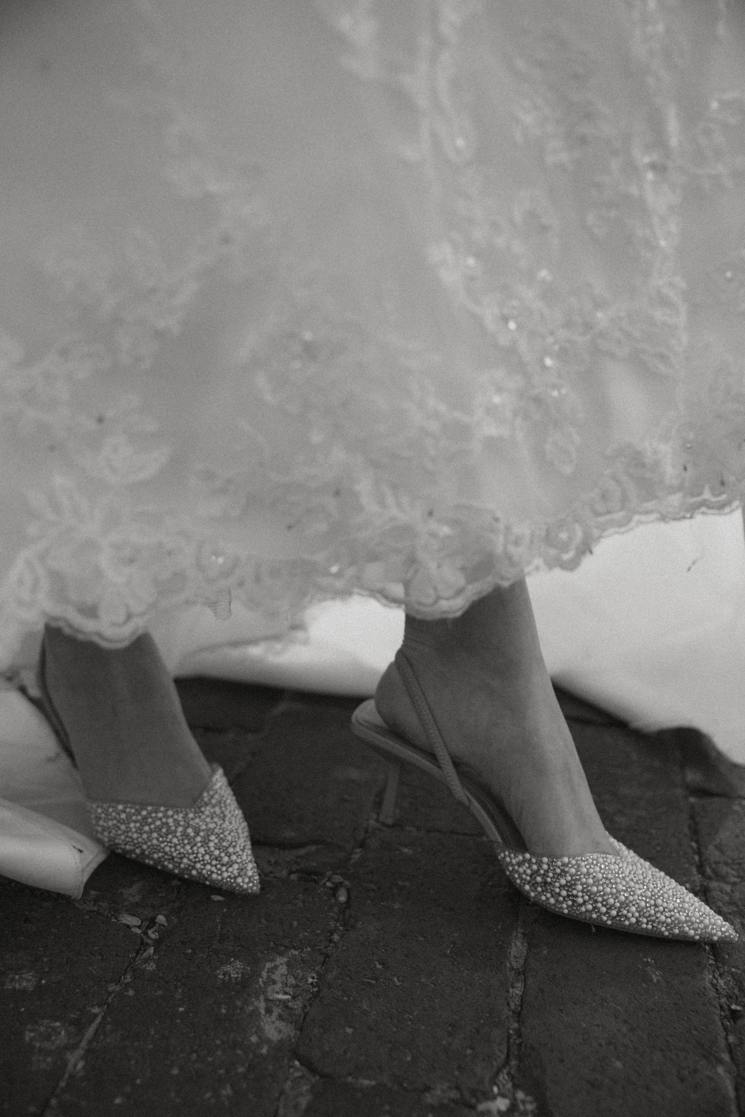 Close-up of a person's feet wearing pointed shoes with a polka dot pattern, standing on cracked ground, with a knotted shoelace visible.