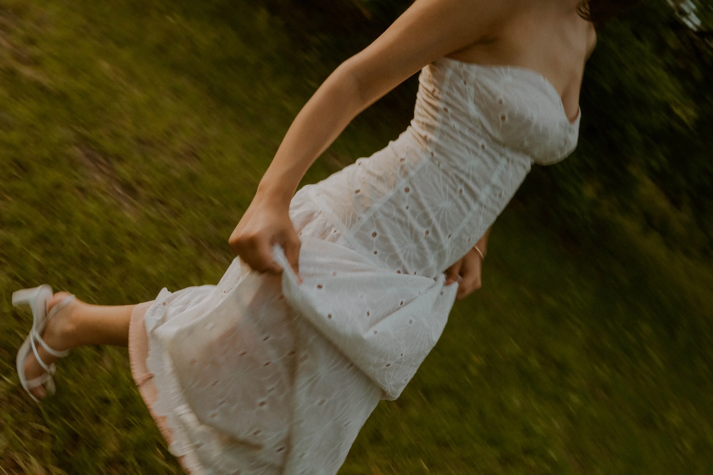 A person running in a white dress with eyelet pattern on grassy ground.