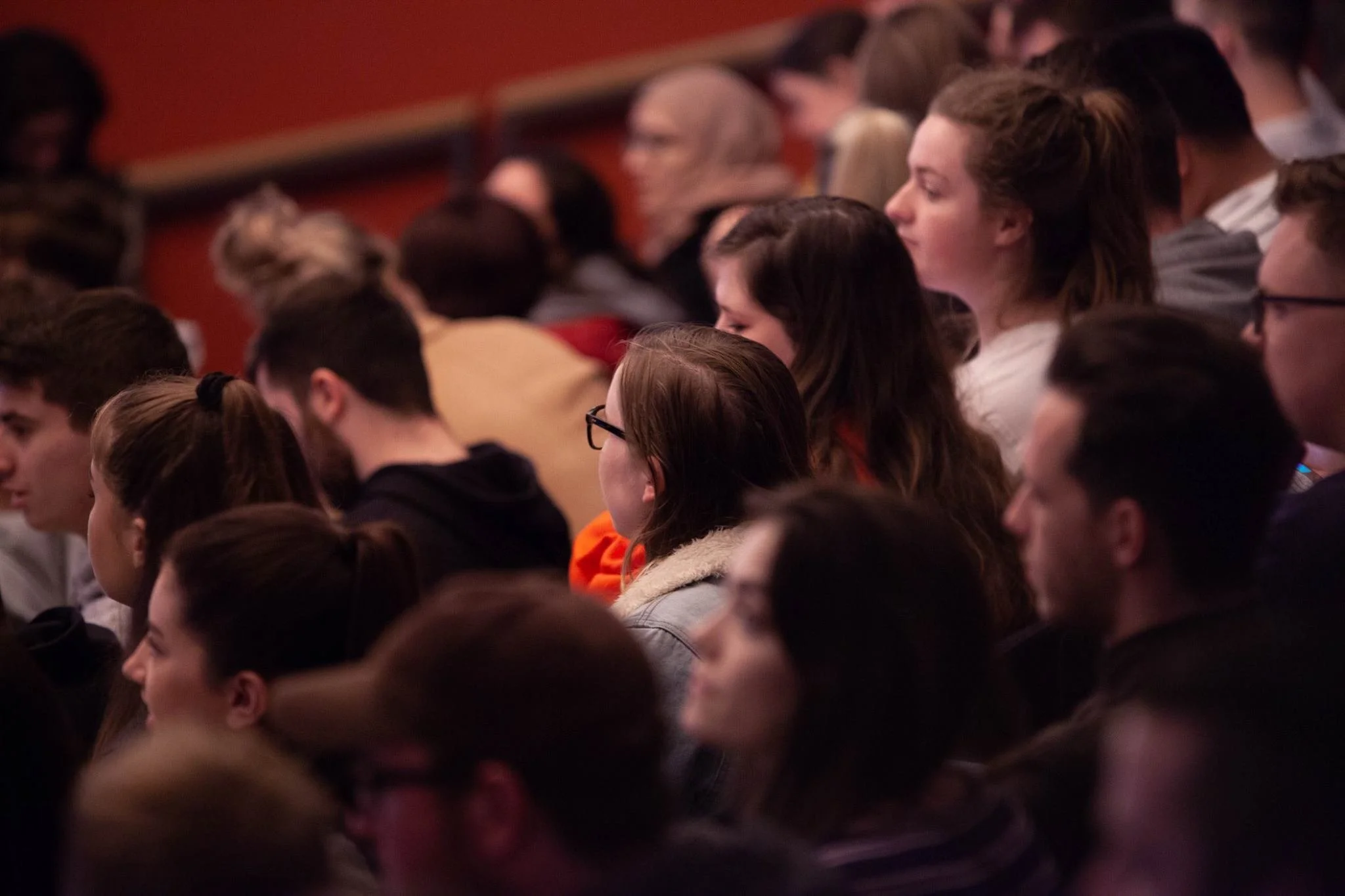 Audience of young people sitting in a theater, watching a presentation or performance.