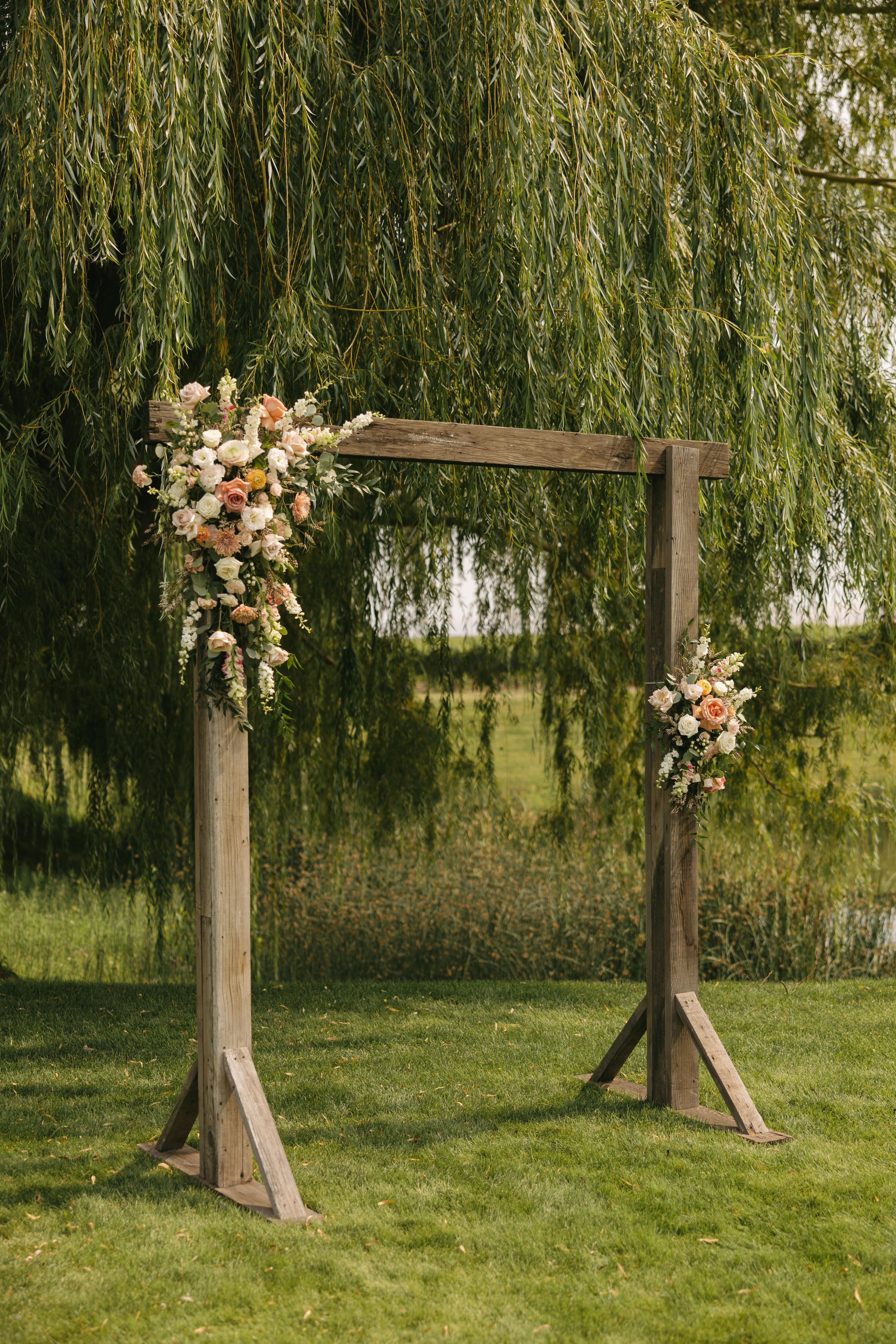 Soft blush, peach, and sage wedding with roses, poppy pods, calcynia, eucalyptus, ranunculus, dahlias at Gooseridge Winery Park Benton City WA. Ceremony Arch flowers