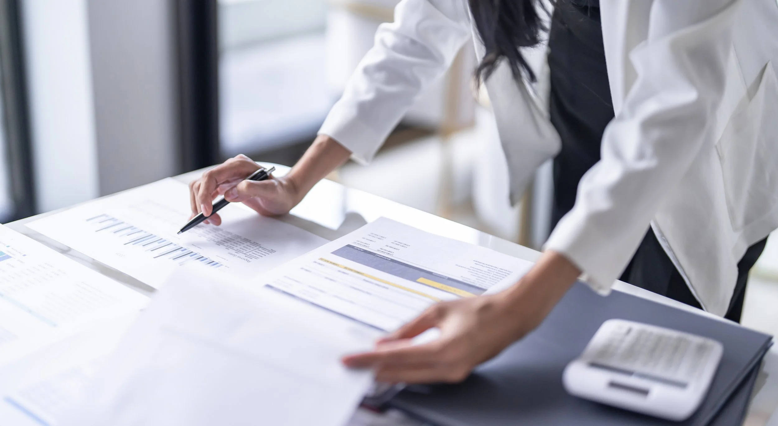 person pointing with pen and reviewing papers with graphs and statistics
