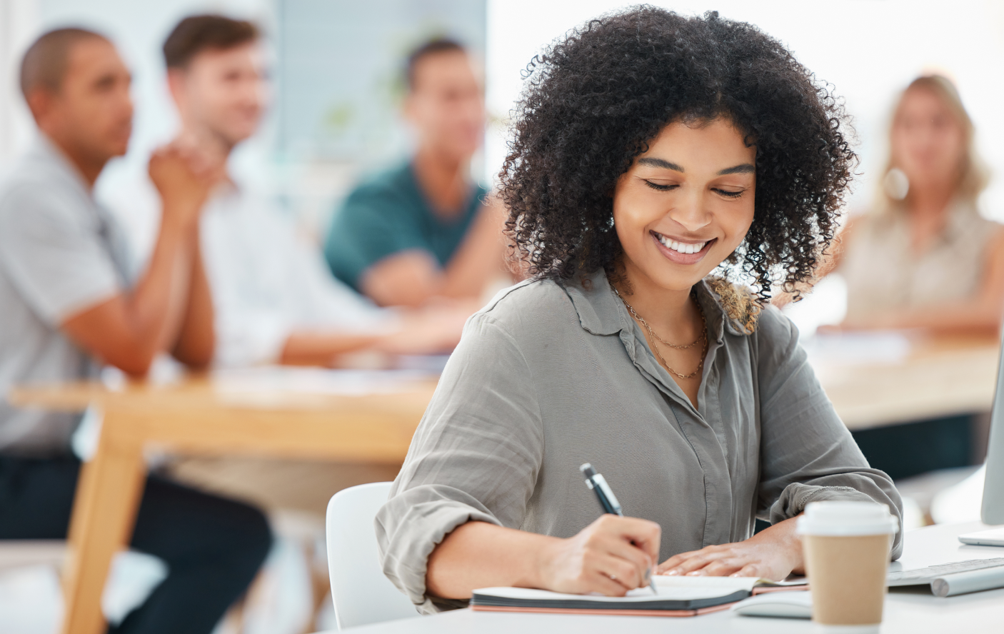 smiling woman sitting in class, writing notes in her notebook