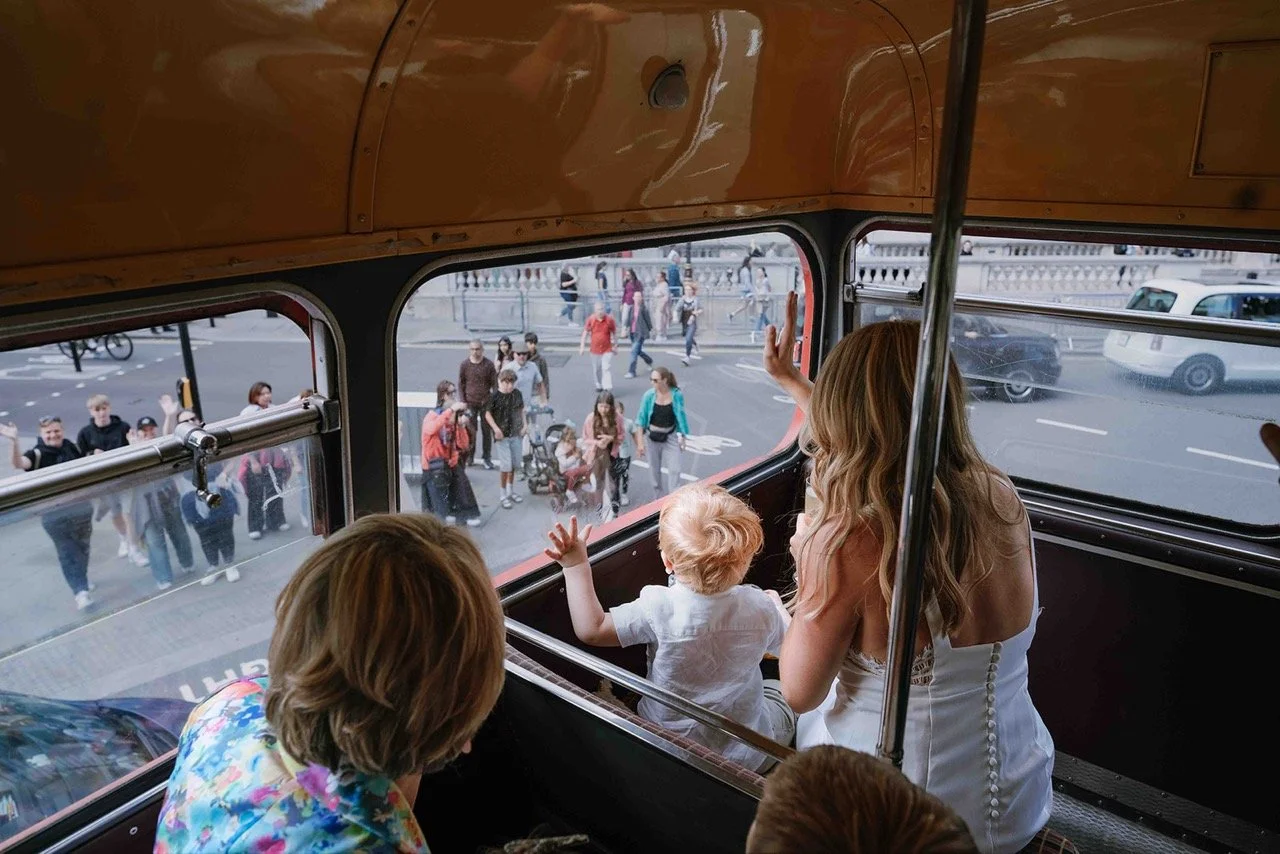 People riding a double-decker bus, with a woman and two children looking out the window at a busy city street with pedestrians and cars.
