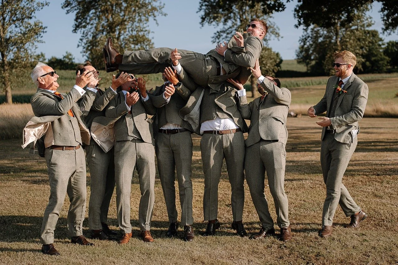 Men in suits celebrating outdoors by lifting a man in a suit over their heads