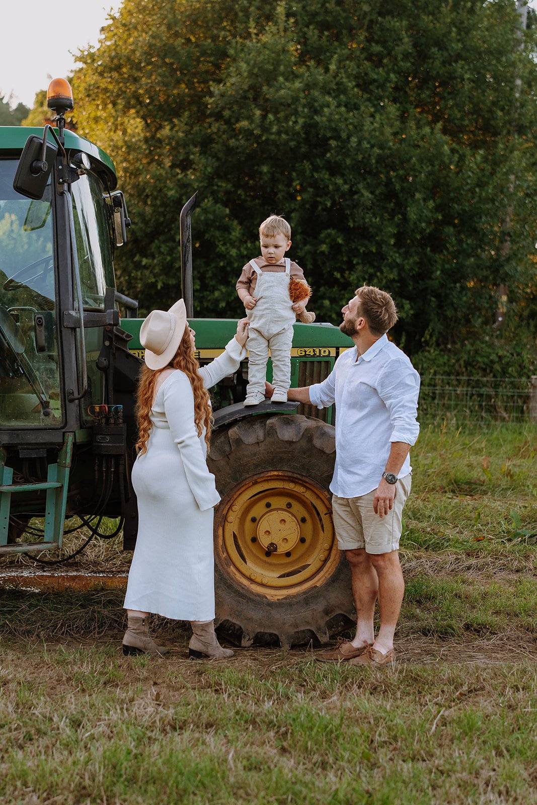 Family with a small boy on a tractor in a grassy field during sunset