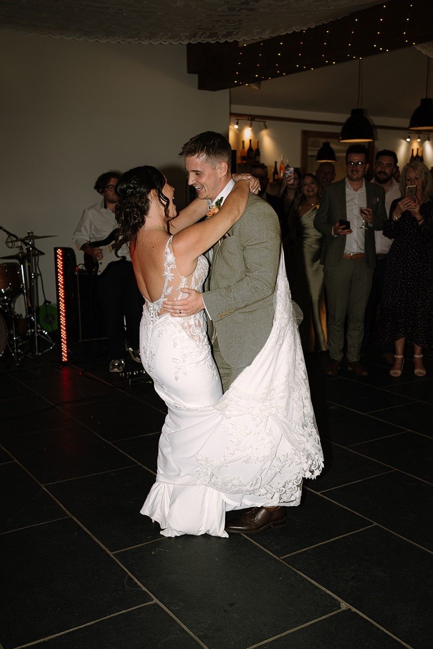 Bride and groom dancing during their wedding reception, with guests watching and taking photos in the background.