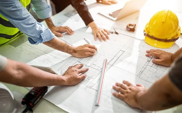 Multiple hands on a building blueprint demonstrating Foresight's Integrative Design service